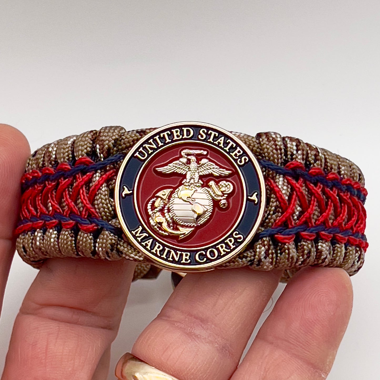 Thick and comfortable braided United States Marine Corps bracelet featuring a 24K gold and silver plated USMC officer Eagle Globe and Anchor medallion, a gold Cobra style tactical buckle and woven with Desert Camo 550 paracord and Imperial Red and Navy Blue micro cord.