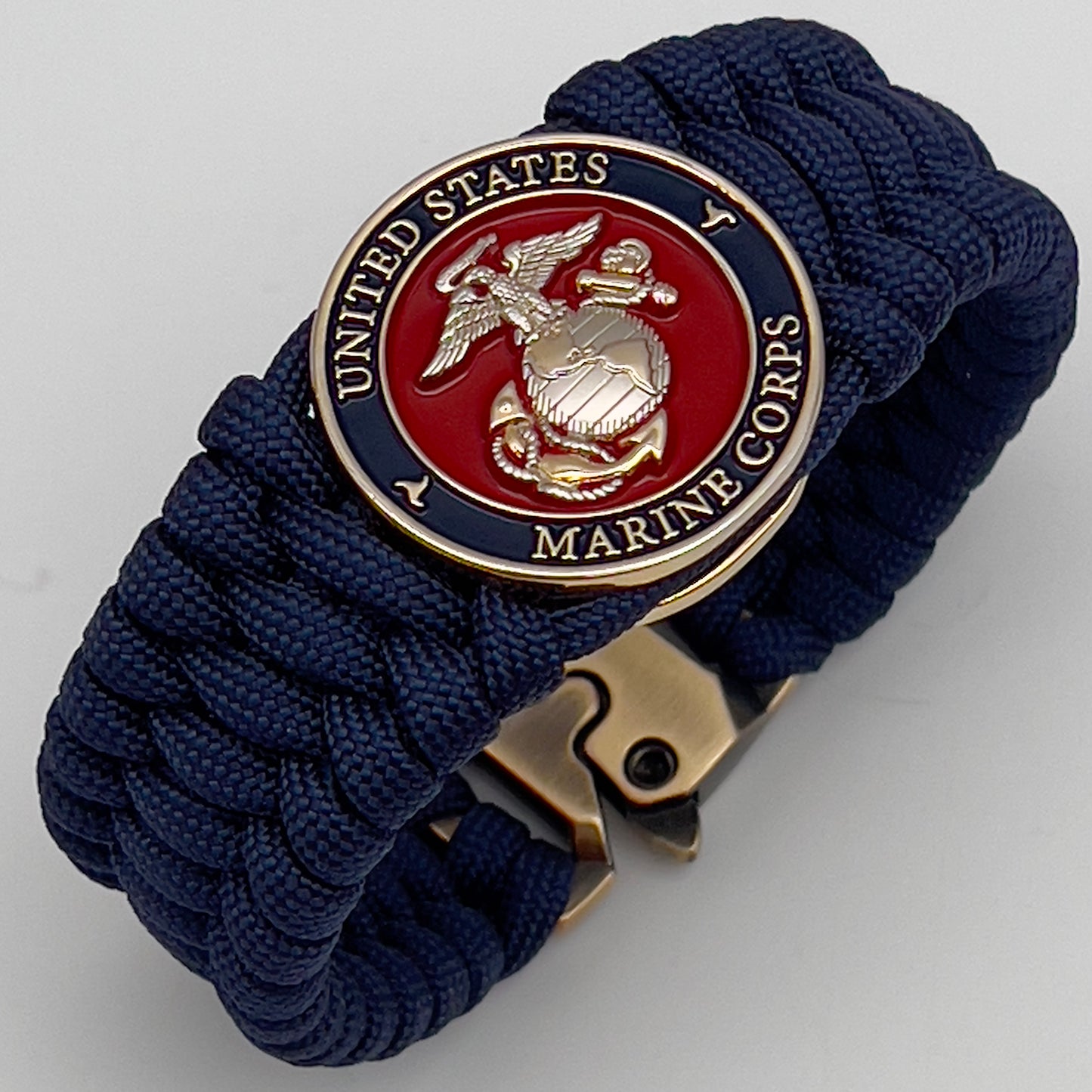 Thick and comfortable braided United States Marine Corps bracelet featuring a 24K gold and silver plated USMC officer Eagle Globe and Anchor medallion, a Cobra style tactical buckle and woven with Navy Blue 550 paracord.