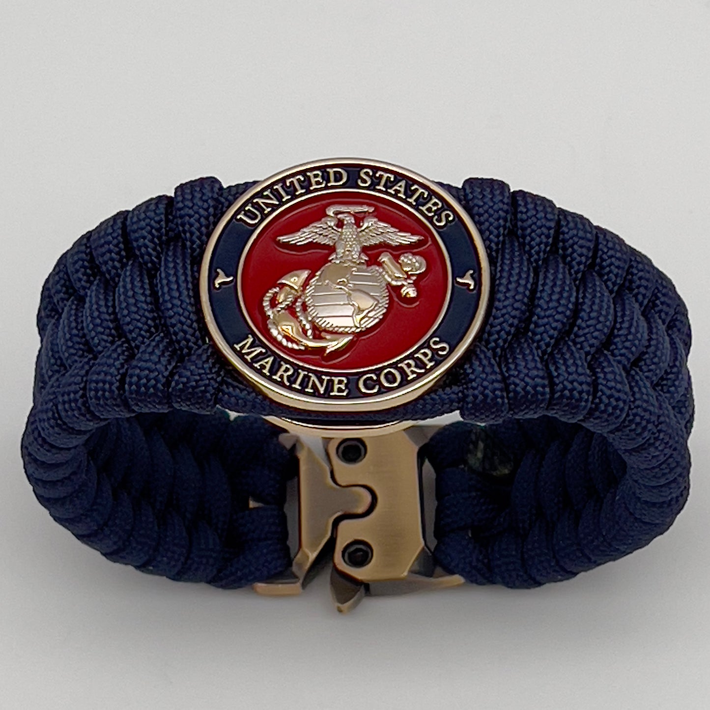 Thick and comfortable braided United States Marine Corps bracelet featuring a 24K gold and silver plated USMC officer Eagle Globe and Anchor medallion, a Cobra style tactical buckle and woven with Navy Blue 550 paracord.