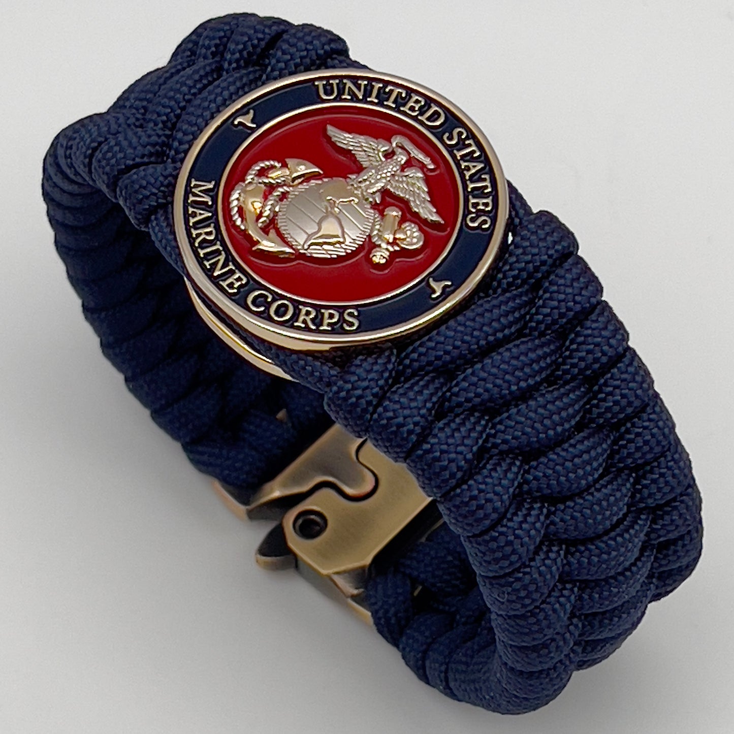 Thick and comfortable braided United States Marine Corps bracelet featuring a 24K gold and silver plated USMC officer Eagle Globe and Anchor medallion, a Cobra style tactical buckle and woven with Navy Blue 550 paracord.