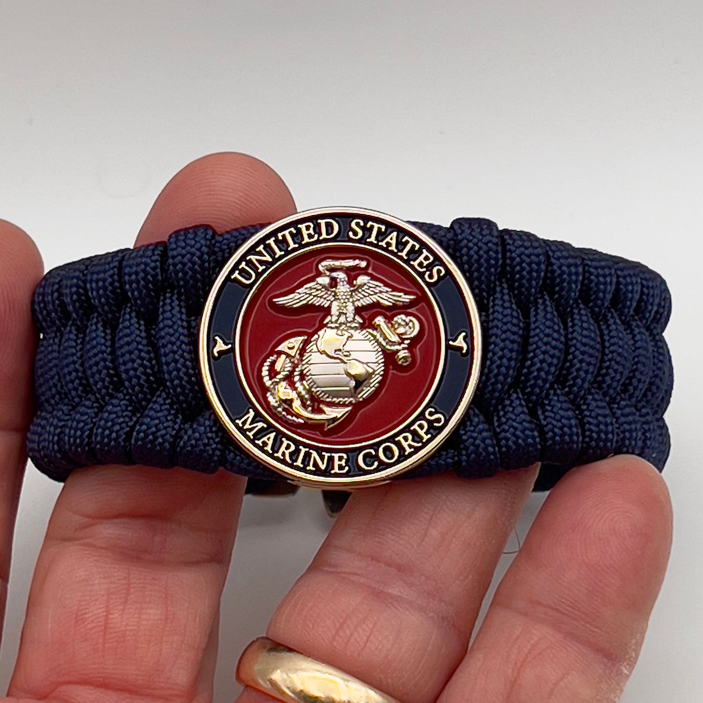 Thick and comfortable braided United States Marine Corps bracelet featuring a 24K gold and silver plated USMC officer Eagle Globe and Anchor medallion, a Cobra style tactical buckle and woven with Navy Blue 550 paracord.