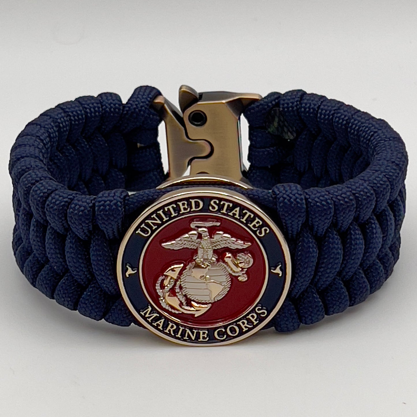 Thick and comfortable braided United States Marine Corps bracelet featuring a 24K gold and silver plated USMC officer Eagle Globe and Anchor medallion, a Cobra style tactical buckle and woven with Navy Blue 550 paracord.