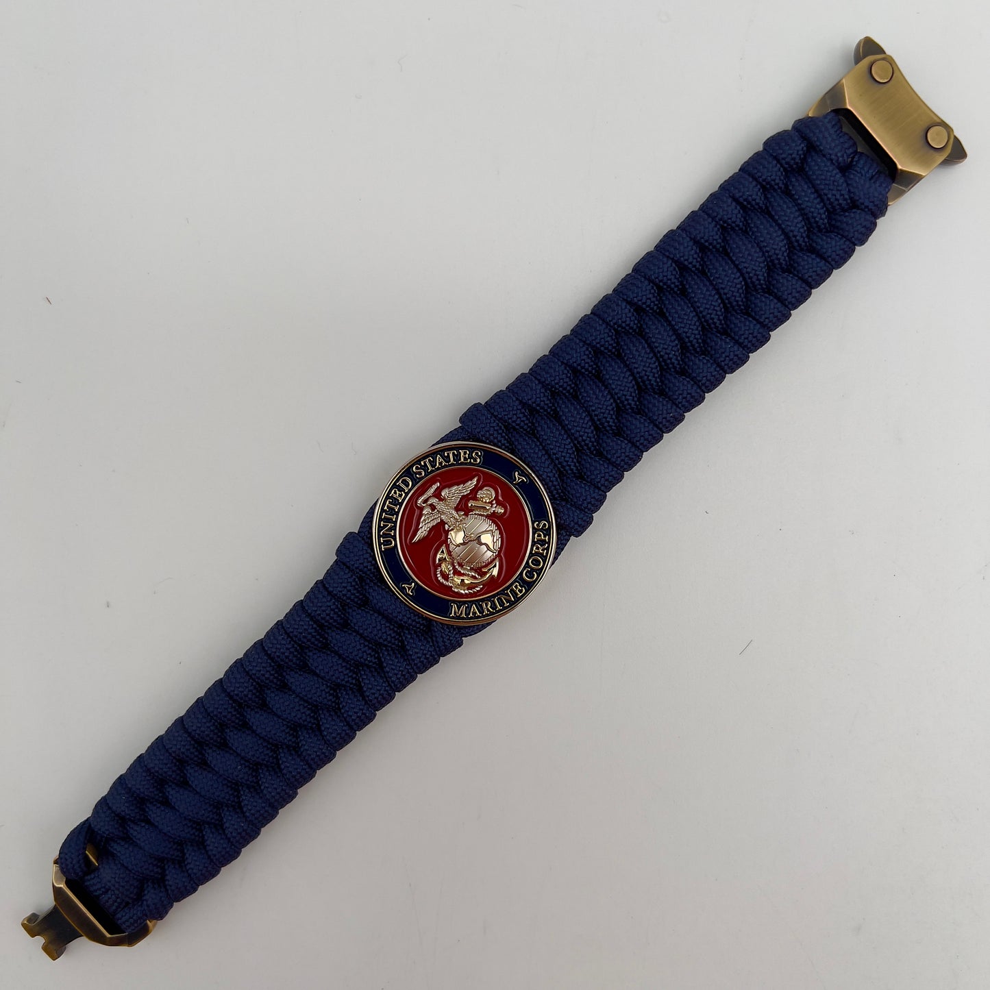 Thick and comfortable braided United States Marine Corps bracelet featuring a 24K gold and silver plated USMC officer Eagle Globe and Anchor medallion, a Cobra style tactical buckle and woven with Navy Blue 550 paracord.