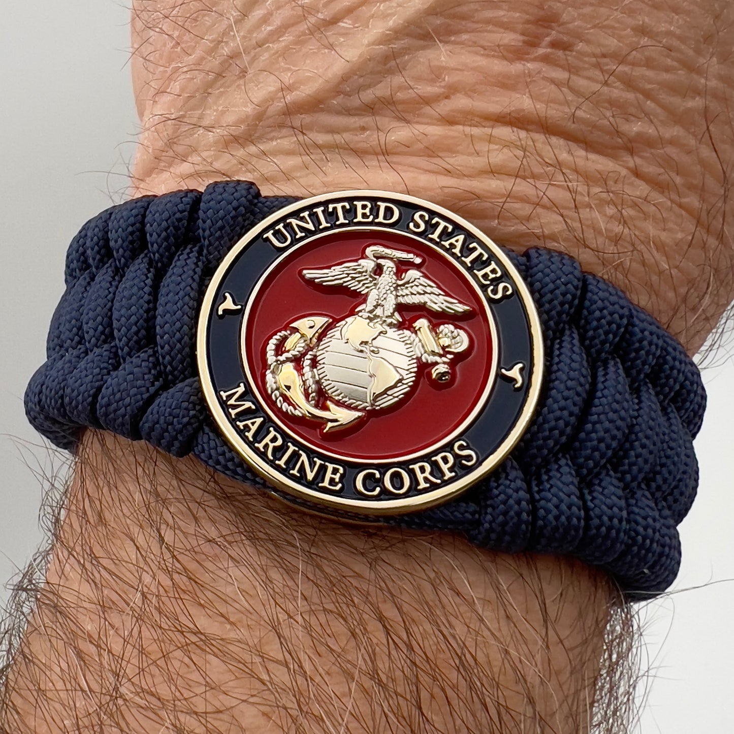 Thick and comfortable braided United States Marine Corps bracelet featuring a 24K gold and silver plated USMC officer Eagle Globe and Anchor medallion, a Cobra style tactical buckle and woven with Navy Blue 550 paracord.