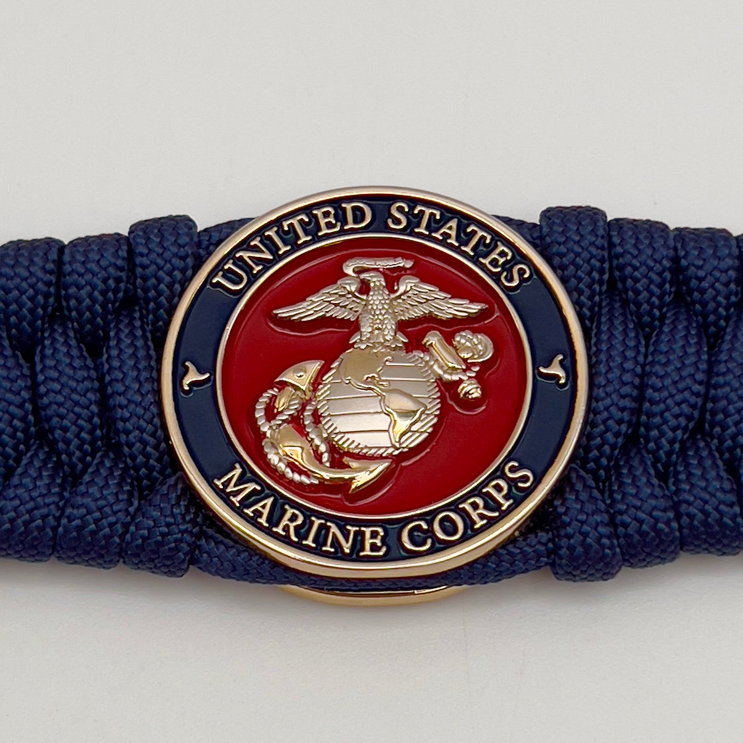 Thick and comfortable braided United States Marine Corps bracelet featuring a 24K gold and silver plated USMC officer Eagle Globe and Anchor medallion, a Cobra style tactical buckle and woven with Navy Blue 550 paracord.