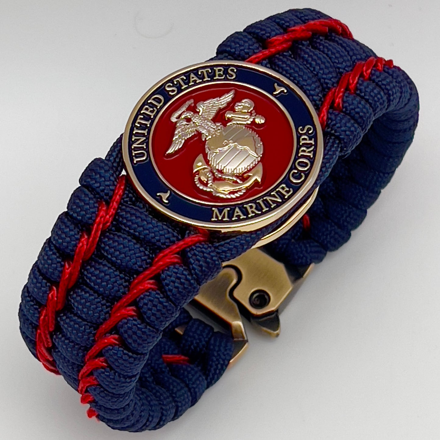 Thick and comfortable braided United States Marine Corps bracelet featuring a 24K gold and silver plated USMC officer Eagle Globe and Anchor medallion, a Cobra style tactical buckle and woven with gold 550 paracord and Imperial Red micro cord.