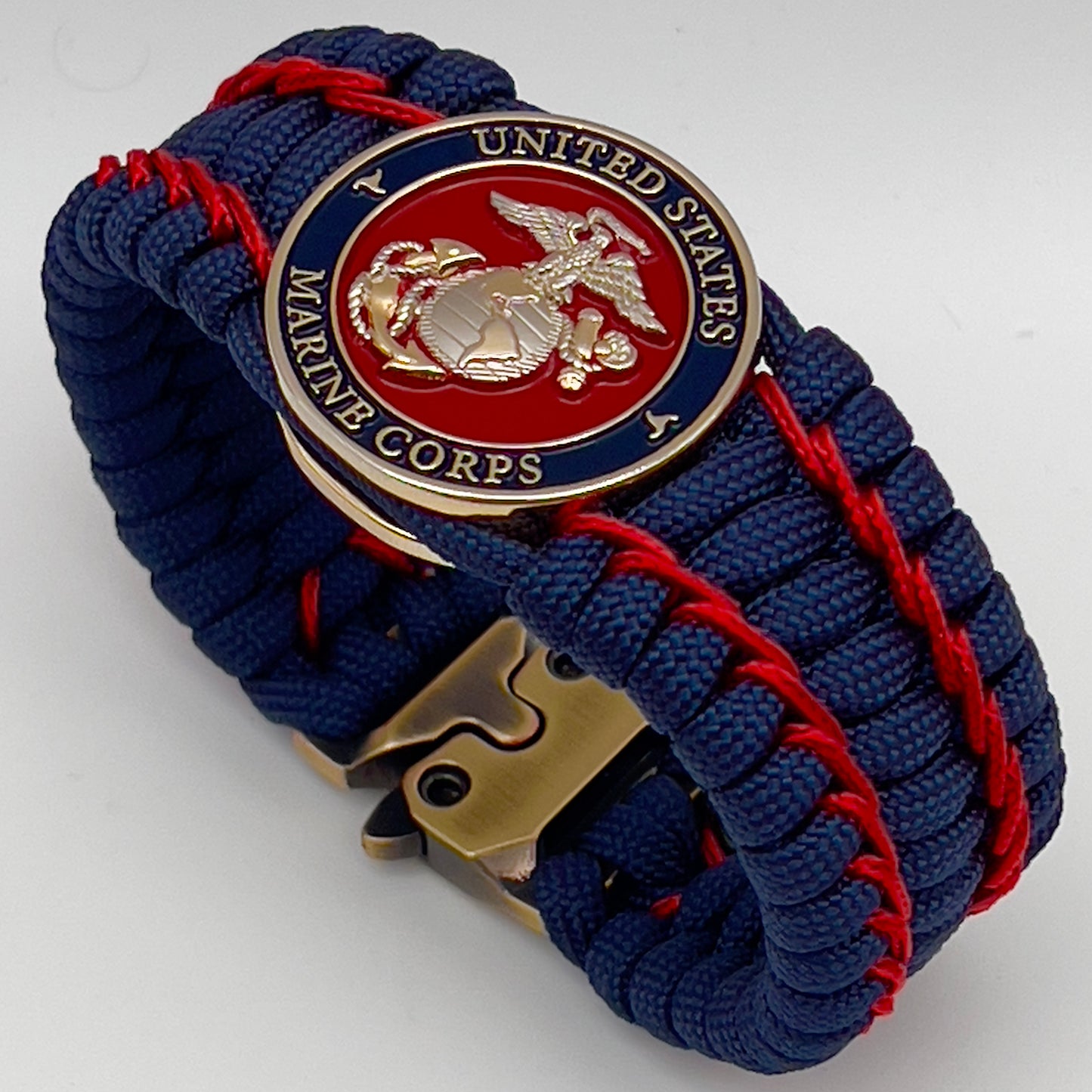 Thick and comfortable braided United States Marine Corps bracelet featuring a 24K gold and silver plated USMC officer Eagle Globe and Anchor medallion, a Cobra style tactical buckle and woven with gold 550 paracord and Imperial Red micro cord.