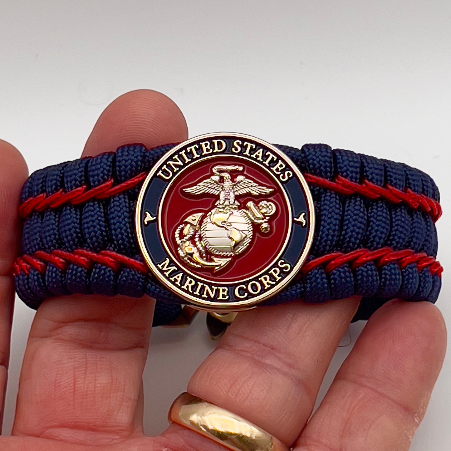 Thick and comfortable braided United States Marine Corps bracelet featuring a 24K gold and silver plated USMC officer Eagle Globe and Anchor medallion, a Cobra style tactical buckle and woven with gold 550 paracord and Imperial Red micro cord.