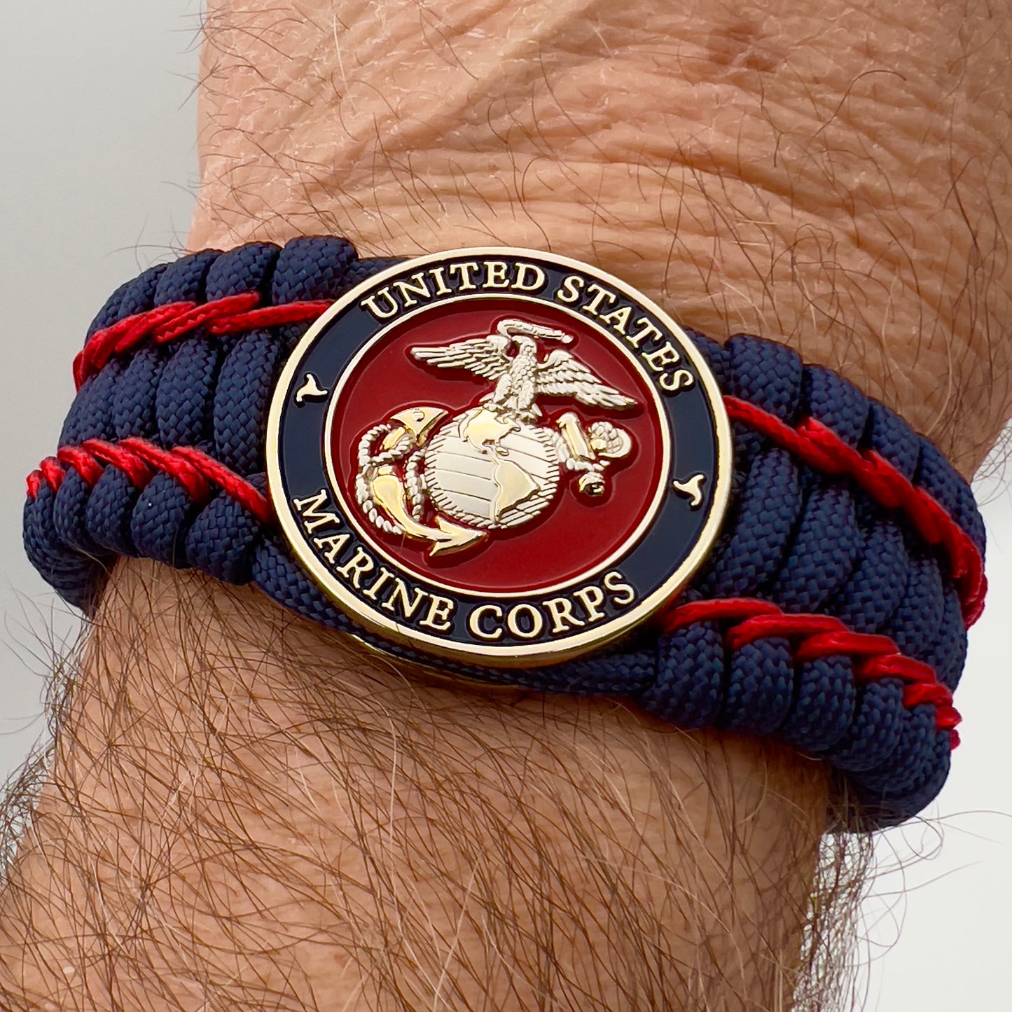 Thick and comfortable braided United States Marine Corps bracelet featuring a 24K gold and silver plated USMC officer Eagle Globe and Anchor medallion, a Cobra style tactical buckle and woven with gold 550 paracord and Imperial Red micro cord.