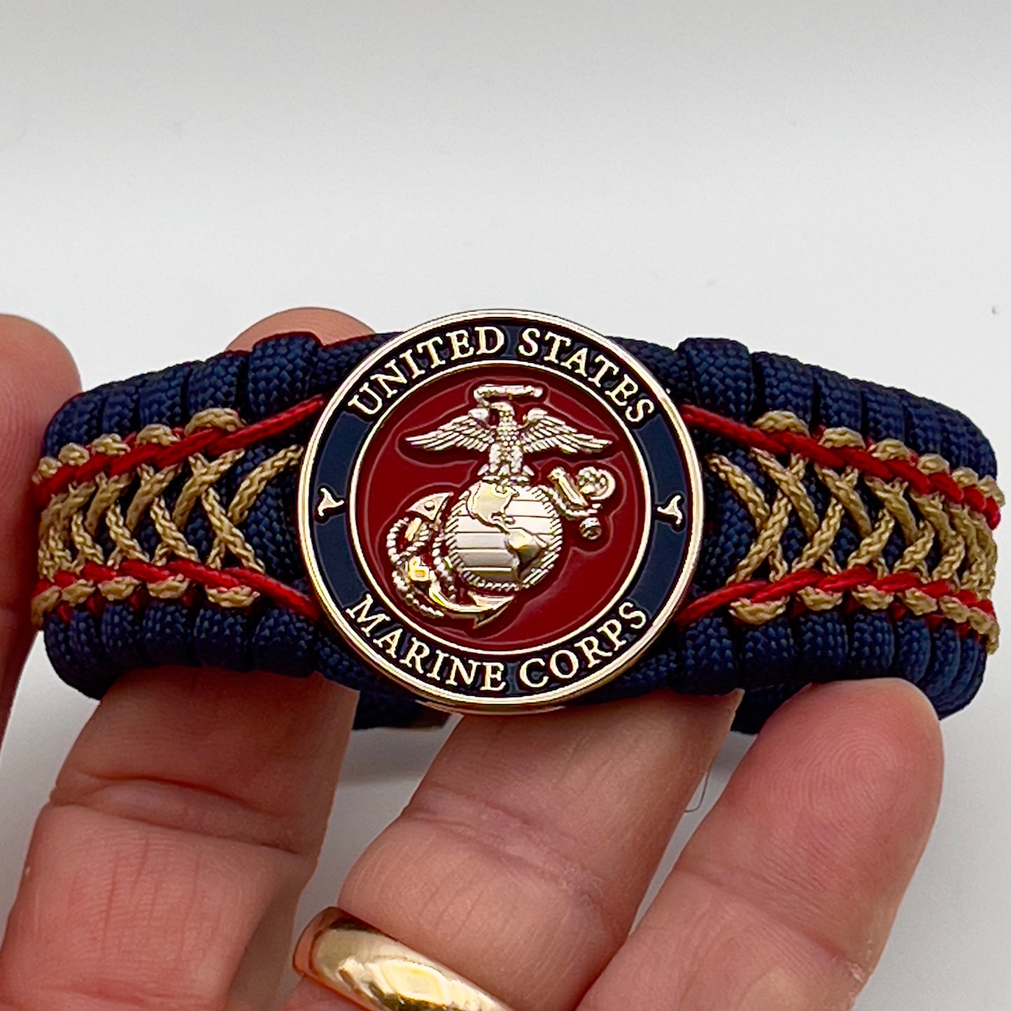Thick and comfortable braided United States Marine Corps bracelet featuring a 24K gold and silver plated USMC officer Eagle Globe and Anchor medallion, a Cobra style tactical buckle and woven with gold 550 paracord and Imperial Red and Gold micro cord.