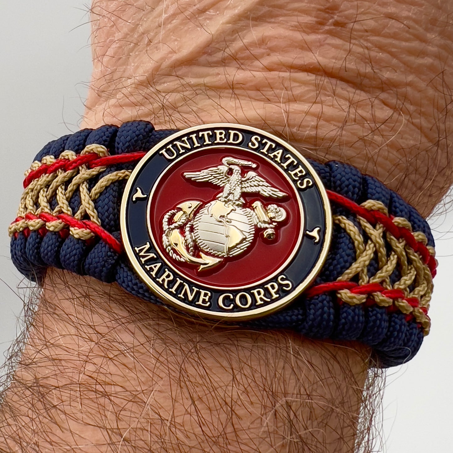 Thick and comfortable braided United States Marine Corps bracelet featuring a 24K gold and silver plated USMC officer Eagle Globe and Anchor medallion, a Cobra style tactical buckle and woven with gold 550 paracord and Imperial Red and Gold micro cord.