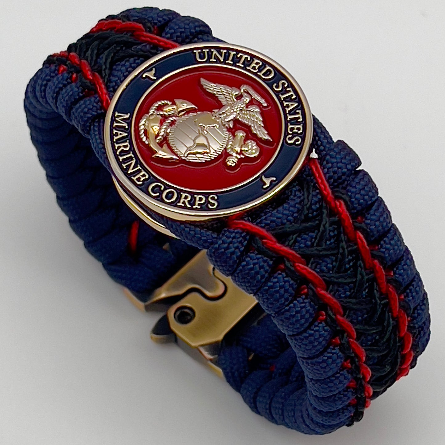 Thick and comfortable braided United States Marine Corps bracelet featuring a 24K gold and silver plated USMC officer Eagle Globe and Anchor medallion, a Cobra style tactical buckle and woven with gold 550 paracord and Imperial Red and Black micro cord.