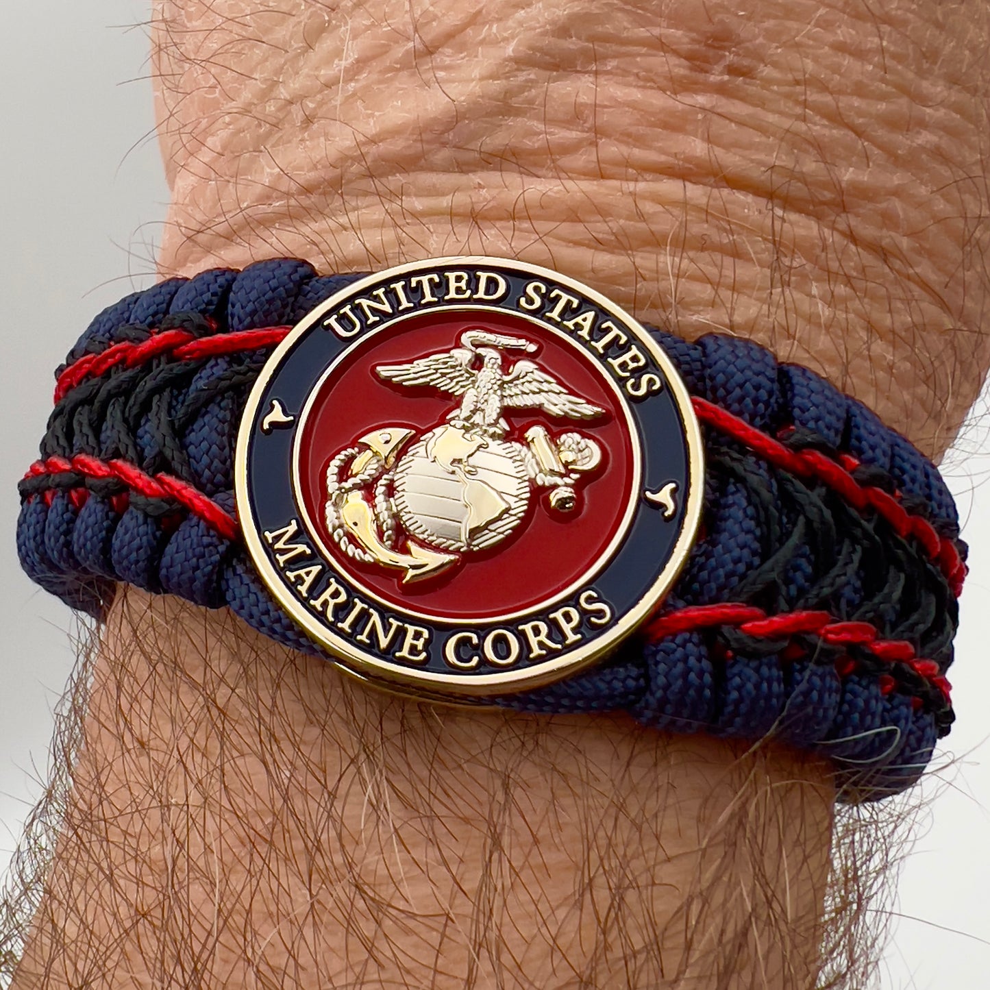 Thick and comfortable braided United States Marine Corps bracelet featuring a 24K gold and silver plated USMC officer Eagle Globe and Anchor medallion, a Cobra style tactical buckle and woven with gold 550 paracord and Imperial Red and Black micro cord.