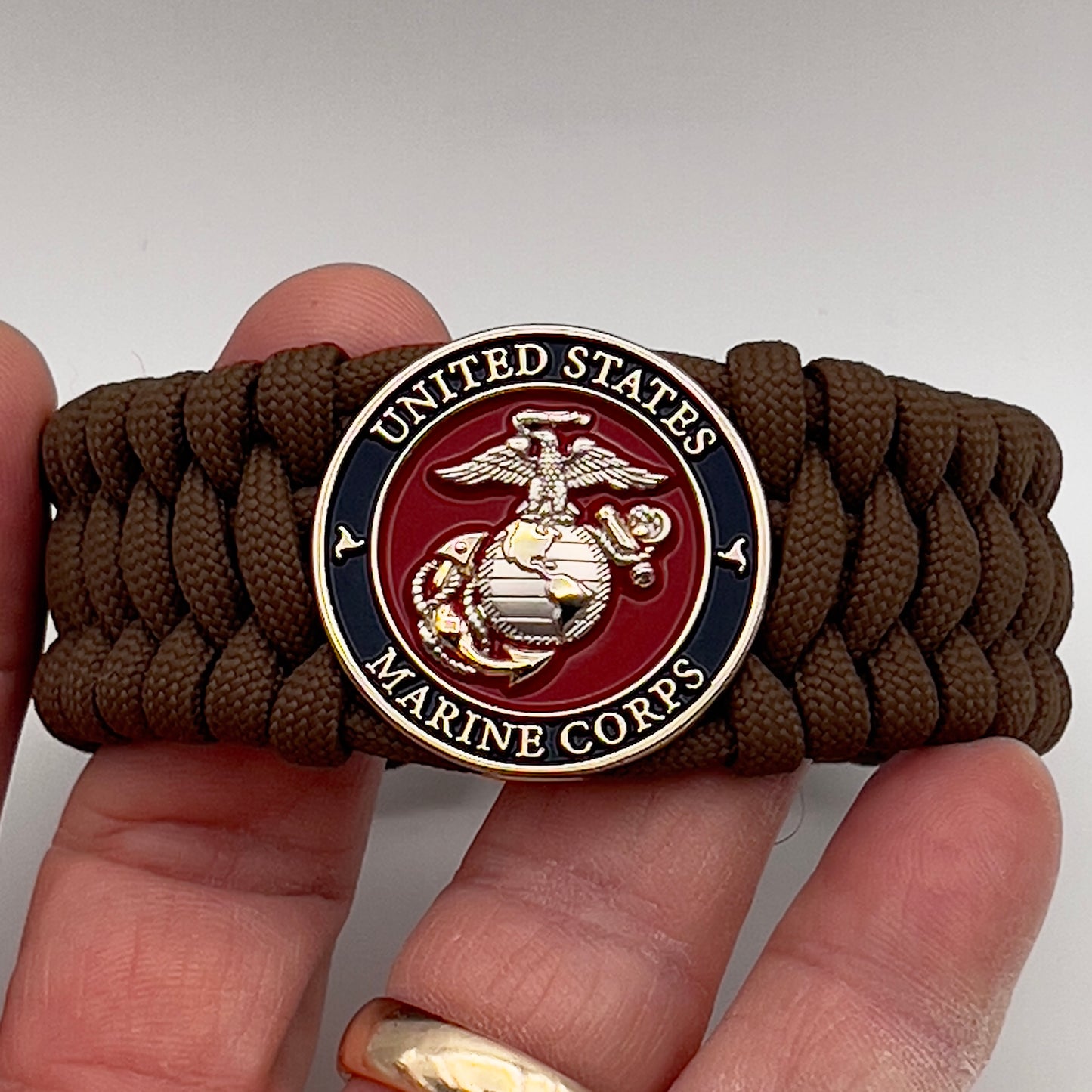 Thick and comfortable braided United States Marine Corps bracelet featuring a 24K gold and silver plated USMC officer Eagle Globe and Anchor medallion, a Cobra style tactical buckle and woven with Coyote Brown 550 paracord.