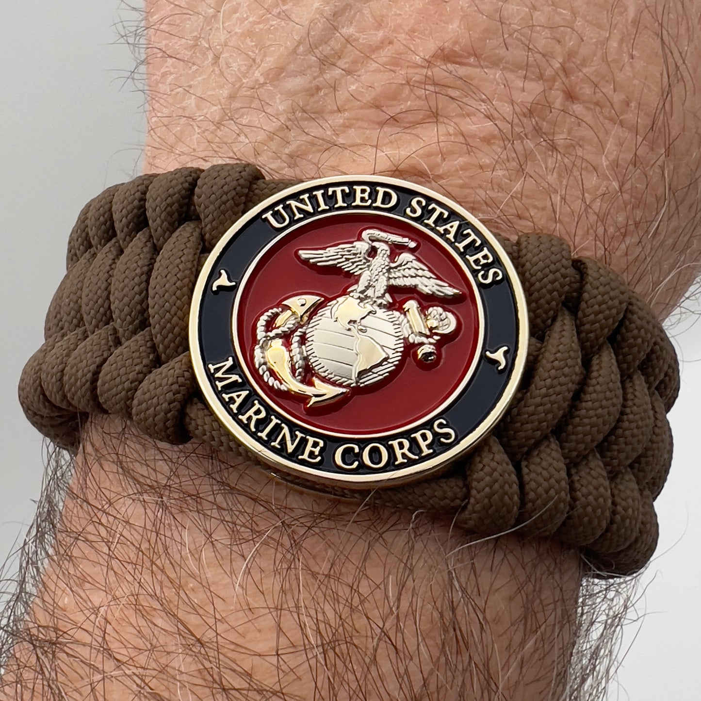Thick and comfortable braided United States Marine Corps bracelet featuring a 24K gold and silver plated USMC officer Eagle Globe and Anchor medallion, a Cobra style tactical buckle and woven with Coyote Brown 550 paracord.