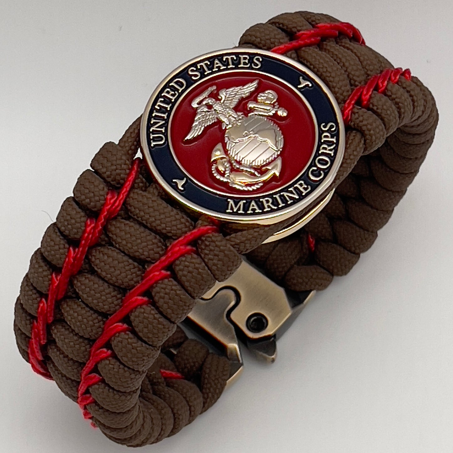 Thick and comfortable braided United States Marine Corps bracelet featuring a 24K gold and silver plated USMC officer Eagle Globe and Anchor medallion, a Cobra style tactical buckle and woven with Coyote Brown 550 paracord and Imperial Red micro cord.