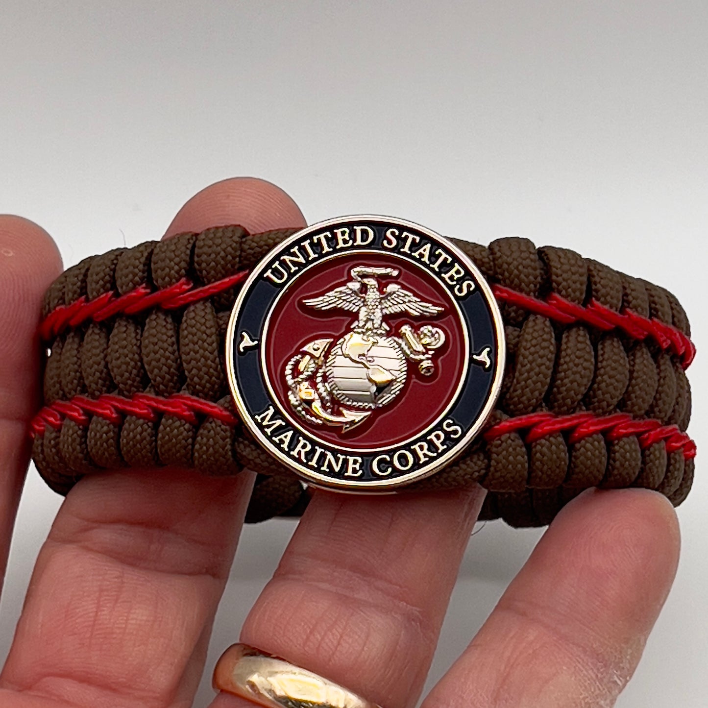 Thick and comfortable braided United States Marine Corps bracelet featuring a 24K gold and silver plated USMC officer Eagle Globe and Anchor medallion, a Cobra style tactical buckle and woven with Coyote Brown 550 paracord and Imperial Red micro cord.