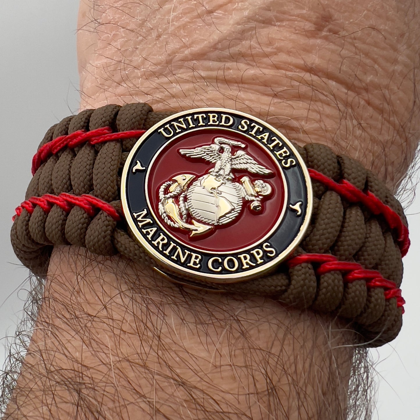 Thick and comfortable braided United States Marine Corps bracelet featuring a 24K gold and silver plated USMC officer Eagle Globe and Anchor medallion, a Cobra style tactical buckle and woven with Coyote Brown 550 paracord and Imperial Red micro cord.