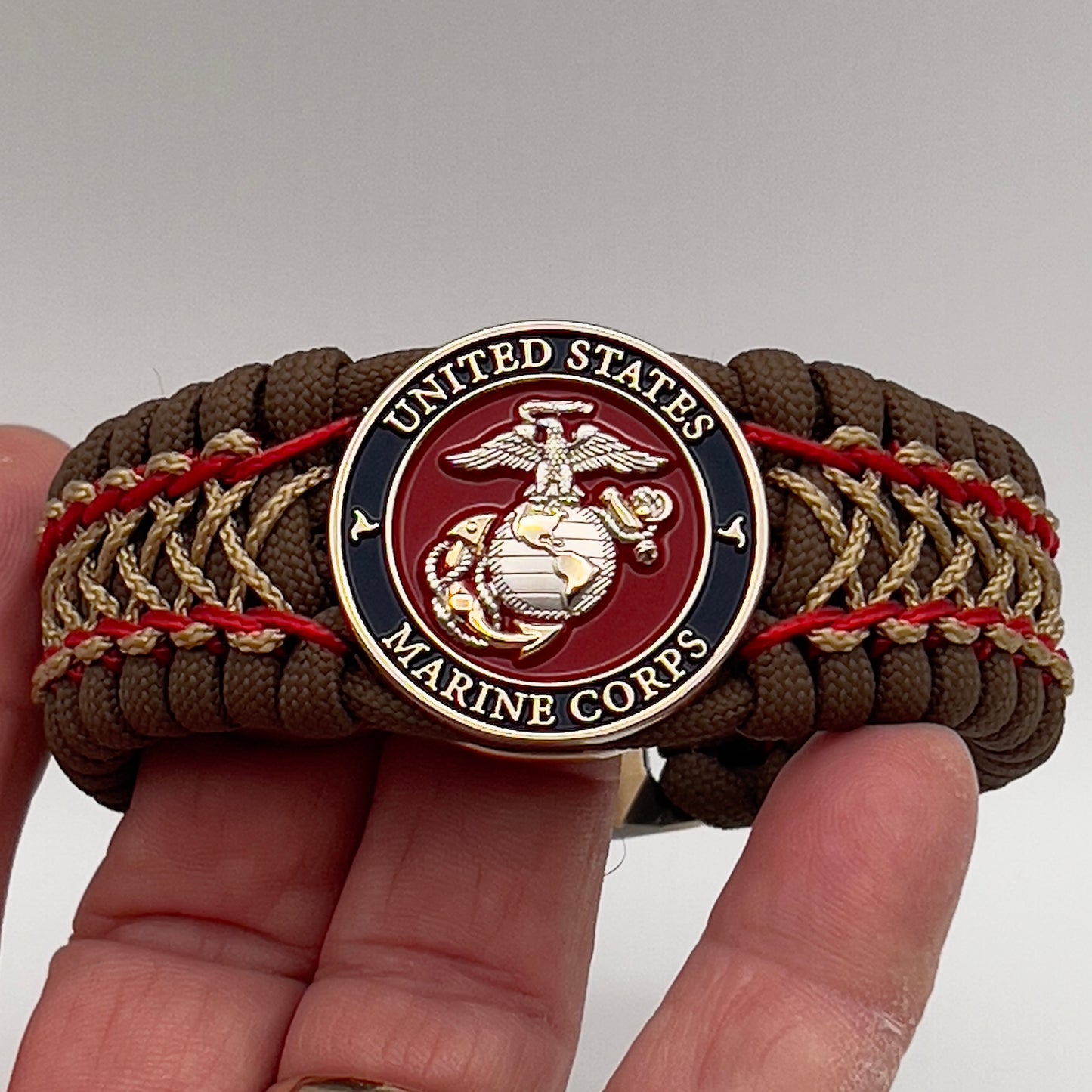 Thick and comfortable braided United States Marine Corps bracelet featuring a 24K gold and silver plated USMC officer Eagle Globe and Anchor medallion, a Cobra style tactical buckle and woven with Coyote Brown 550 paracord and Imperial Red and gold micro cord.