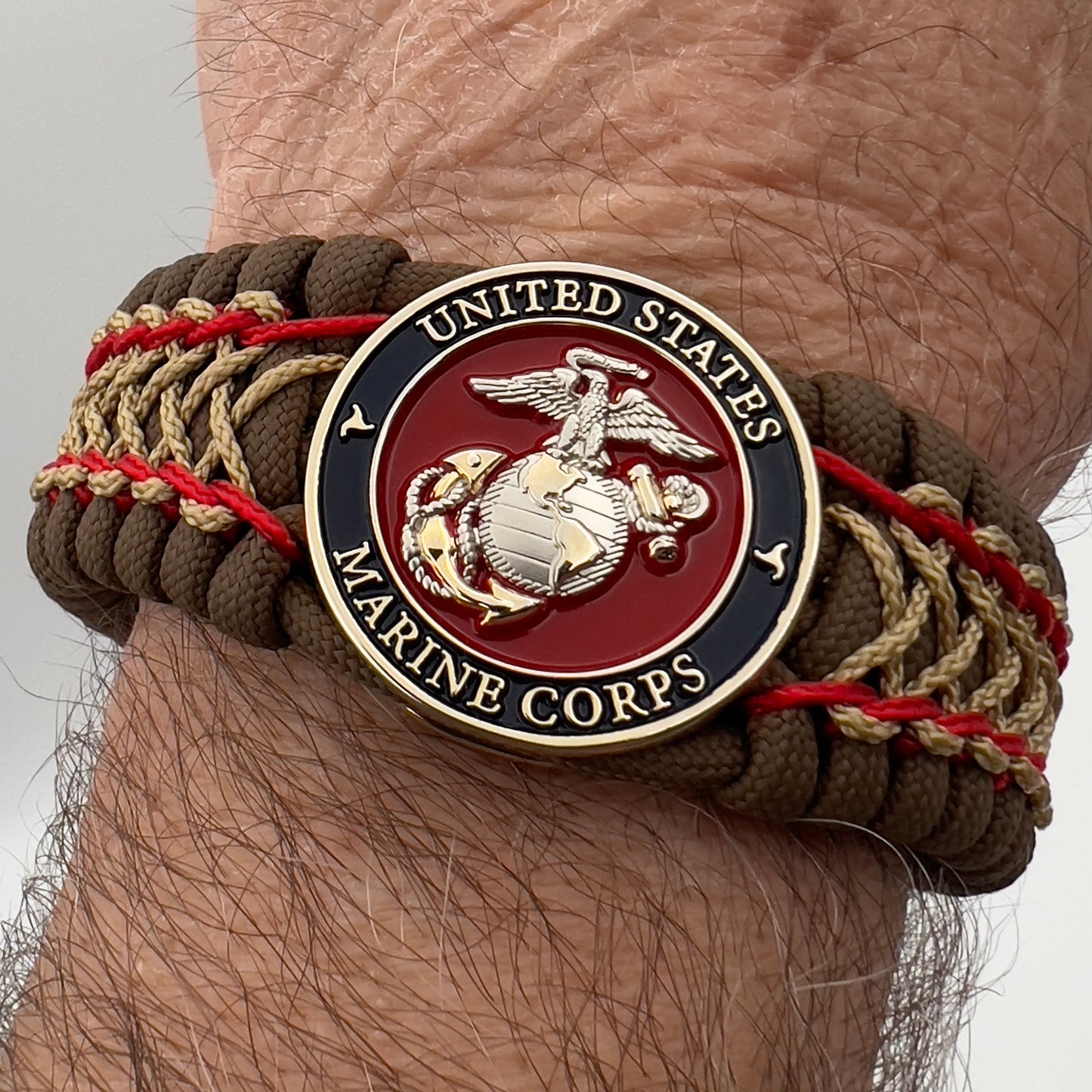 Thick and comfortable braided United States Marine Corps bracelet featuring a 24K gold and silver plated USMC officer Eagle Globe and Anchor medallion, a Cobra style tactical buckle and woven with Coyote Brown 550 paracord and Imperial Red and gold micro cord.