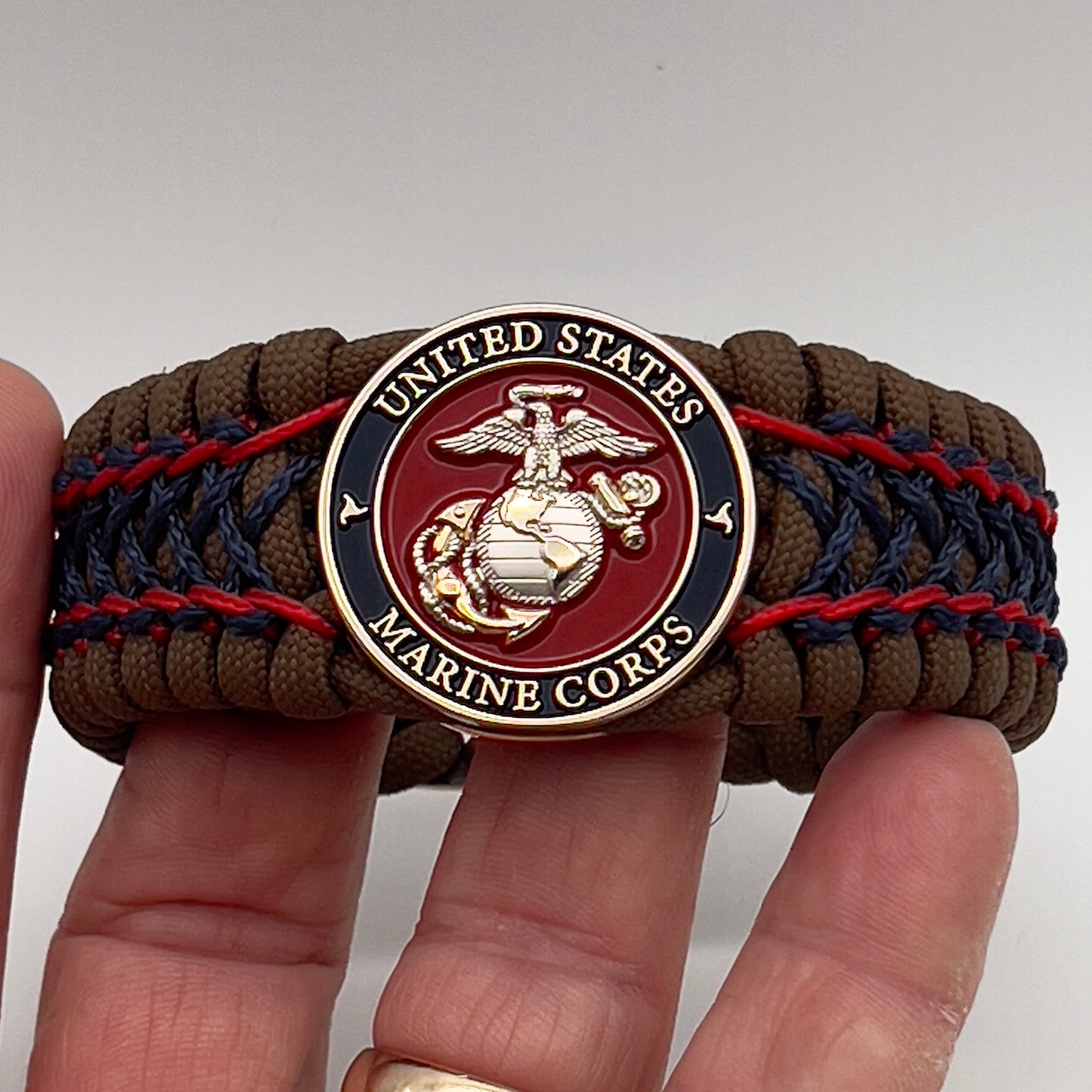 Thick and comfortable braided United States Marine Corps bracelet featuring a 24K gold and silver plated USMC officer Eagle Globe and Anchor medallion, a Cobra style tactical buckle and woven with Coyote Brown 550 paracord and Imperial Red and Navy Blue micro cord.