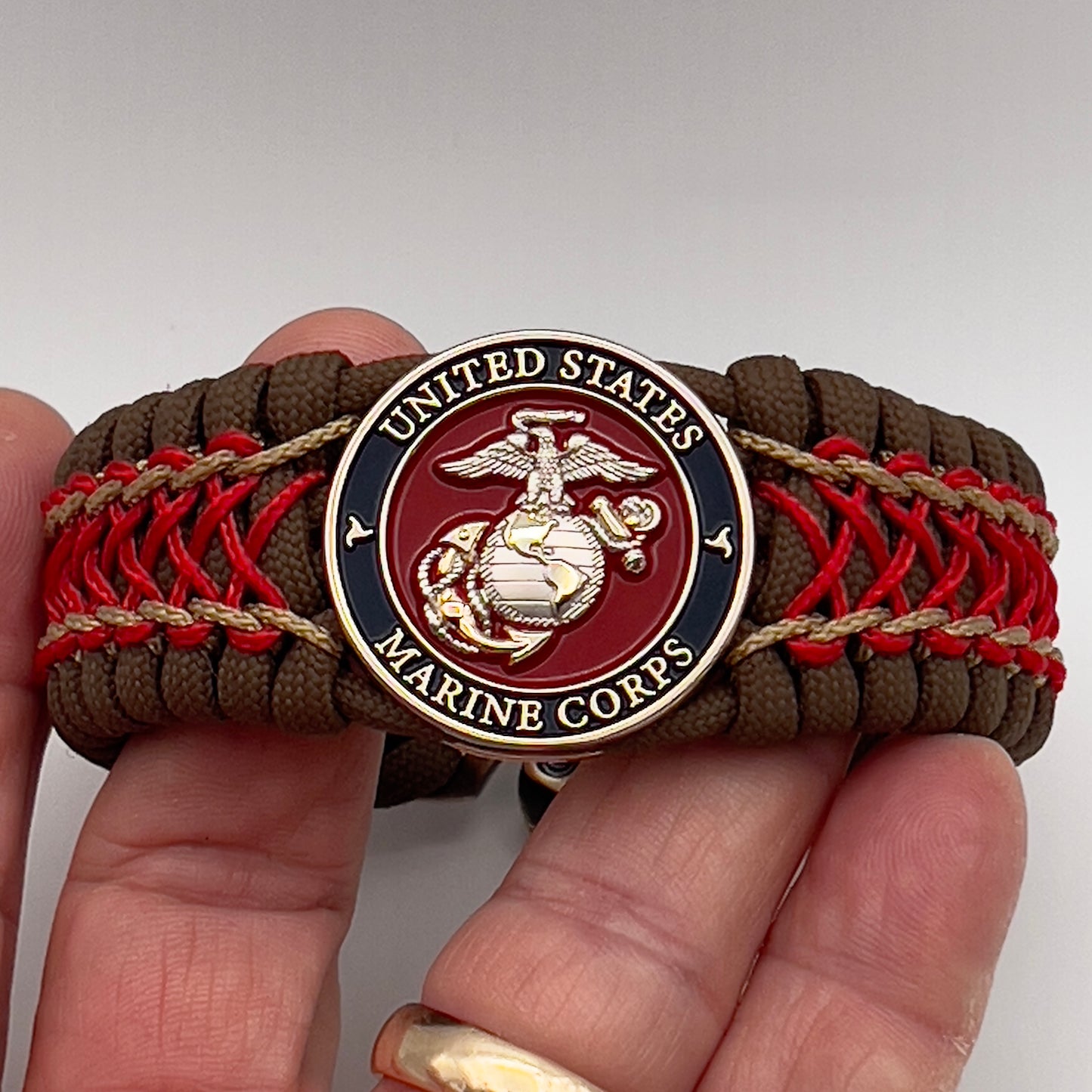 Thick and comfortable braided United States Marine Corps bracelet featuring a 24K gold and silver plated USMC officer Eagle Globe and Anchor medallion, a Cobra style tactical buckle and woven with Coyote Brown 550 paracord and Imperial Red and gold micro cord.