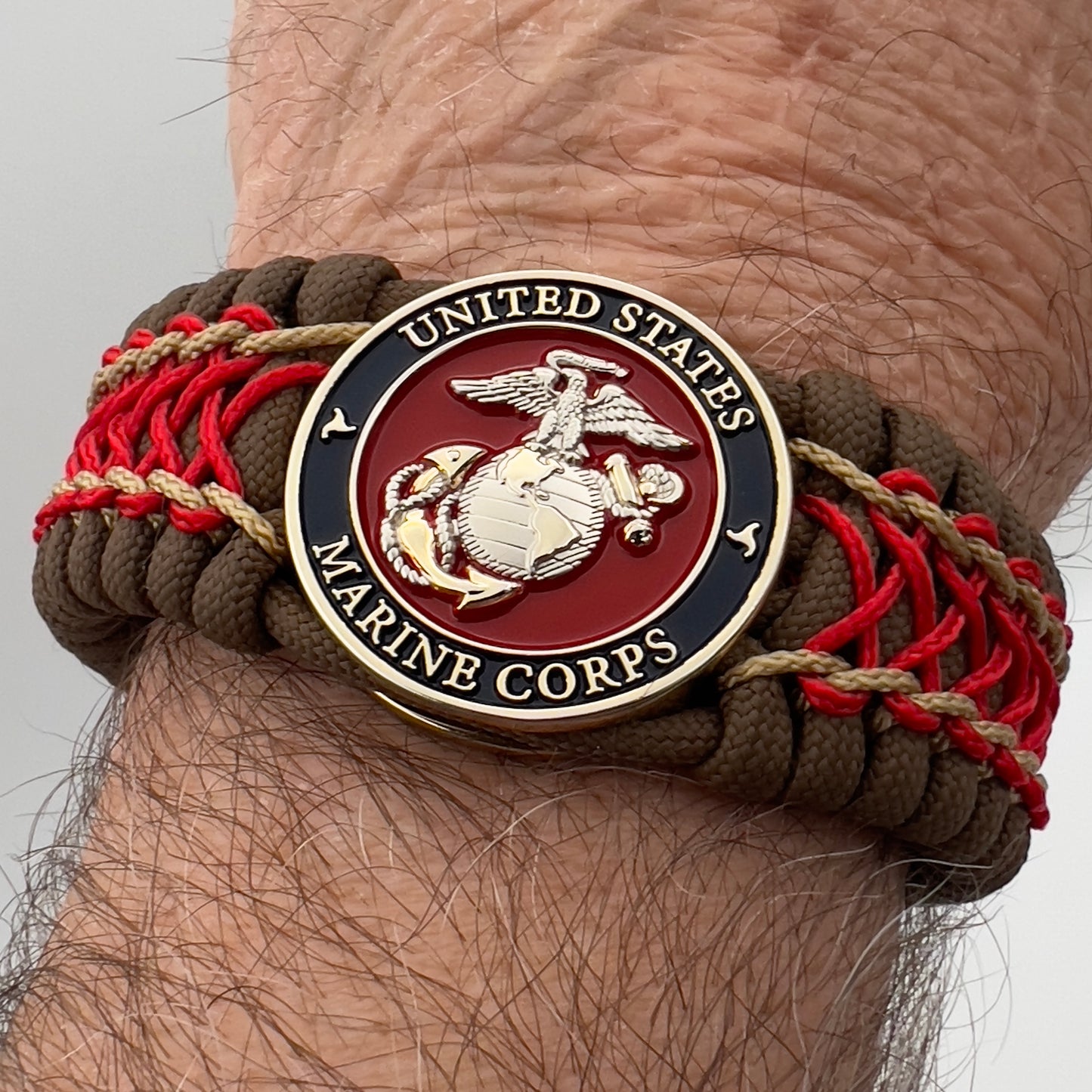 Thick and comfortable braided United States Marine Corps bracelet featuring a 24K gold and silver plated USMC officer Eagle Globe and Anchor medallion, a Cobra style tactical buckle and woven with Coyote Brown 550 paracord and Imperial Red and gold micro cord.
