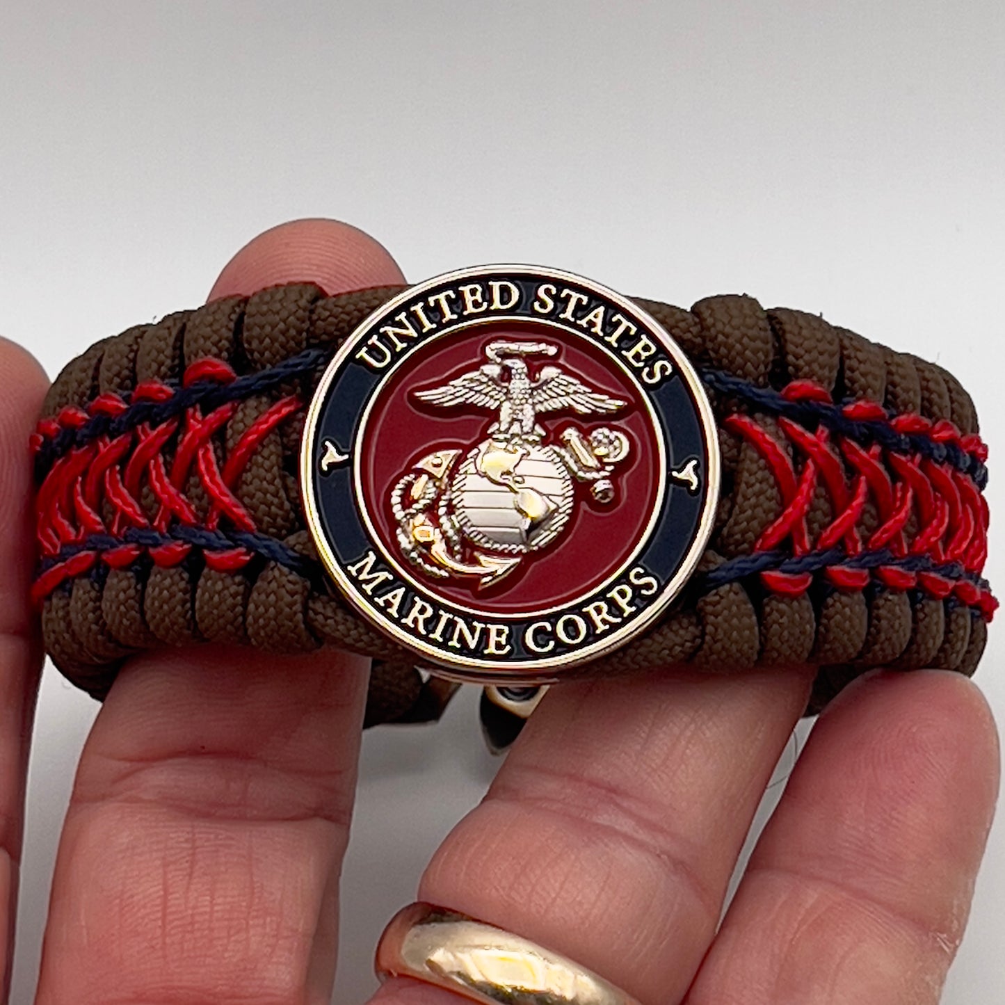 Thick and comfortable braided United States Marine Corps bracelet featuring a 24K gold and silver plated USMC officer Eagle Globe and Anchor medallion, a Cobra style tactical buckle and woven with Coyote Brown 550 paracord and Imperial Red and Navy Blue micro cord.
