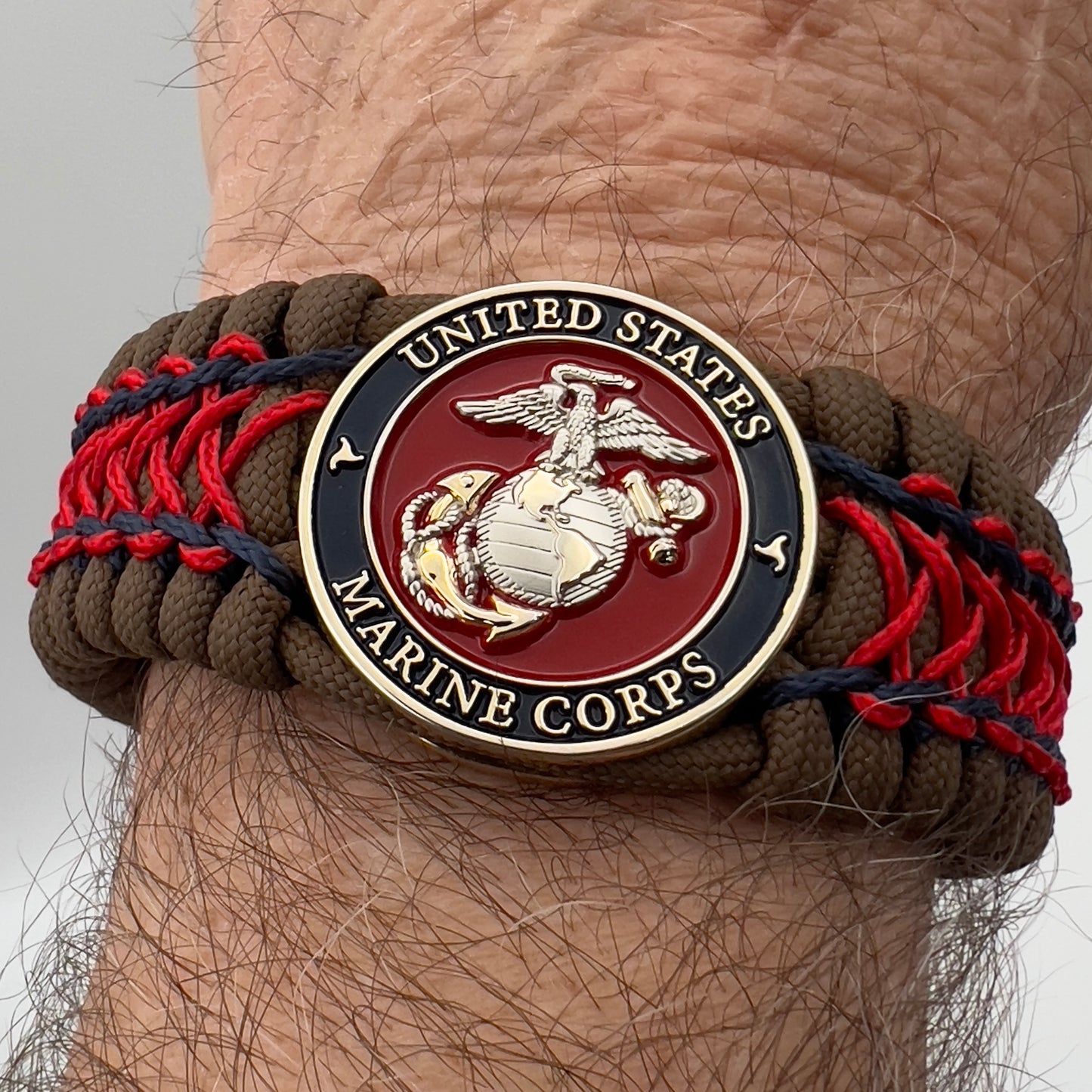 Thick and comfortable braided United States Marine Corps bracelet featuring a 24K gold and silver plated USMC officer Eagle Globe and Anchor medallion, a Cobra style tactical buckle and woven with Coyote Brown 550 paracord and Imperial Red and Navy Blue micro cord.