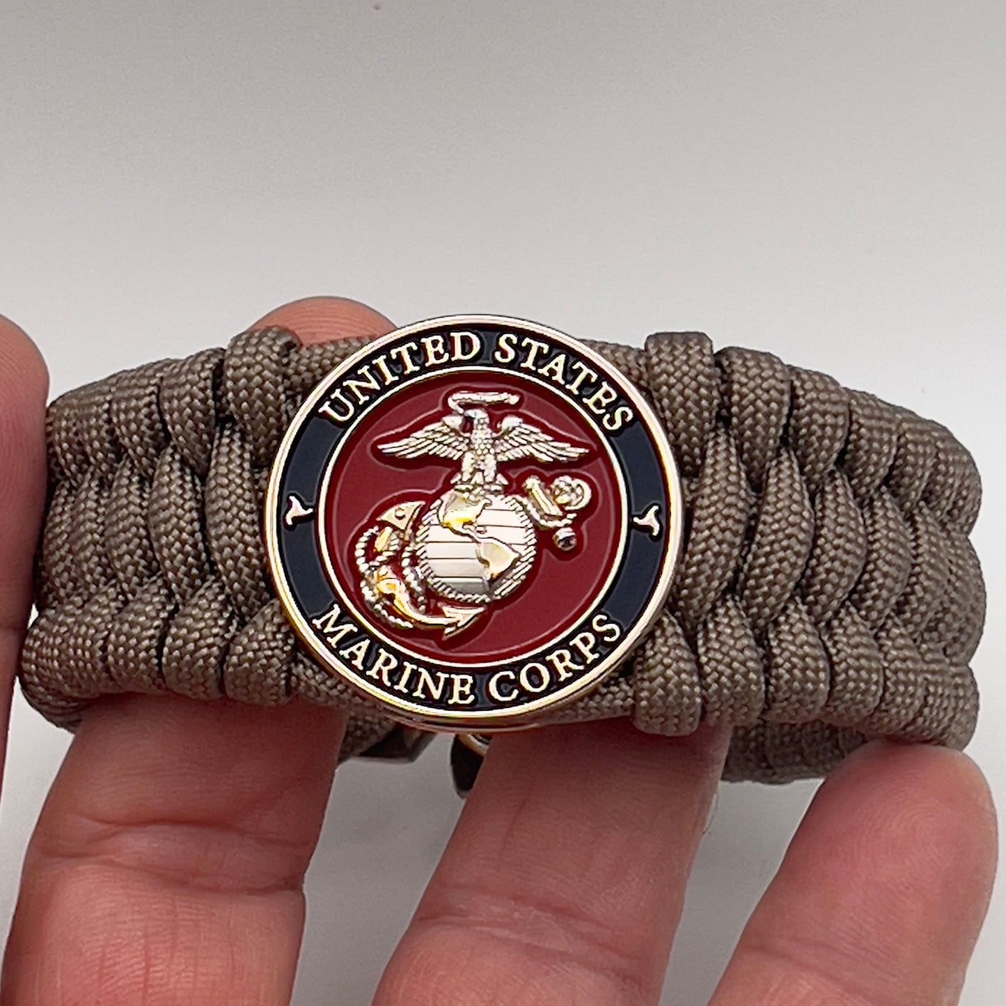 Thick and comfortable braided United States Marine Corps bracelet featuring a 24K gold and silver plated USMC officer Eagle Globe and Anchor medallion, a Cobra style tactical buckle and woven with tan 550 paracord.