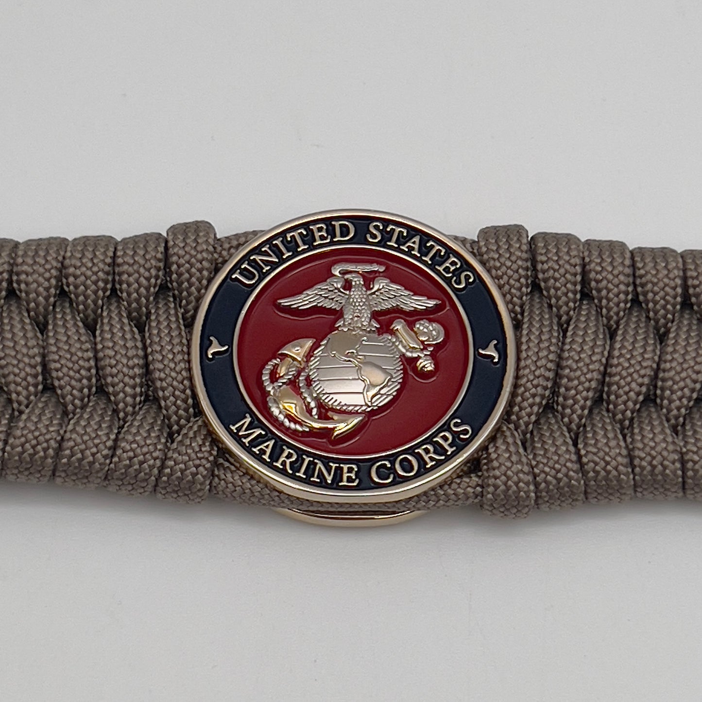 Thick and comfortable braided United States Marine Corps bracelet featuring a 24K gold and silver plated USMC officer Eagle Globe and Anchor medallion, a Cobra style tactical buckle and woven with tan 550 paracord.