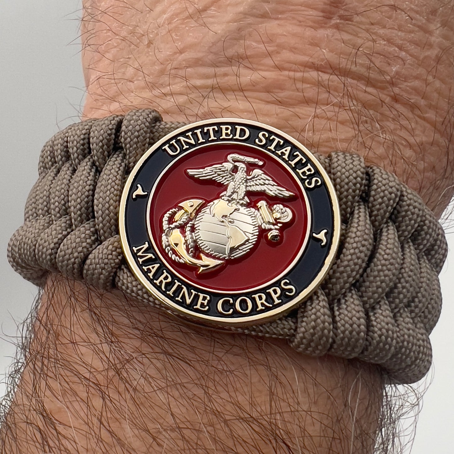 Thick and comfortable braided United States Marine Corps bracelet featuring a 24K gold and silver plated USMC officer Eagle Globe and Anchor medallion, a Cobra style tactical buckle and woven with tan 550 paracord.