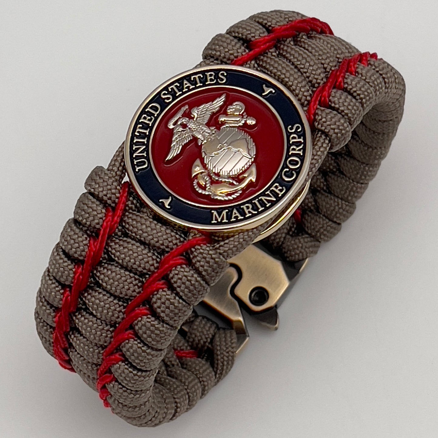 Thick, semi-rigid and comfortable braided United States Marine Corps bracelet featuring a 24K gold and silver plated USMC officer Eagle Globe and Anchor medallion, a gold Cobra style tactical buckle and woven with tan 550 paracord and Imperial Red micro cord.
