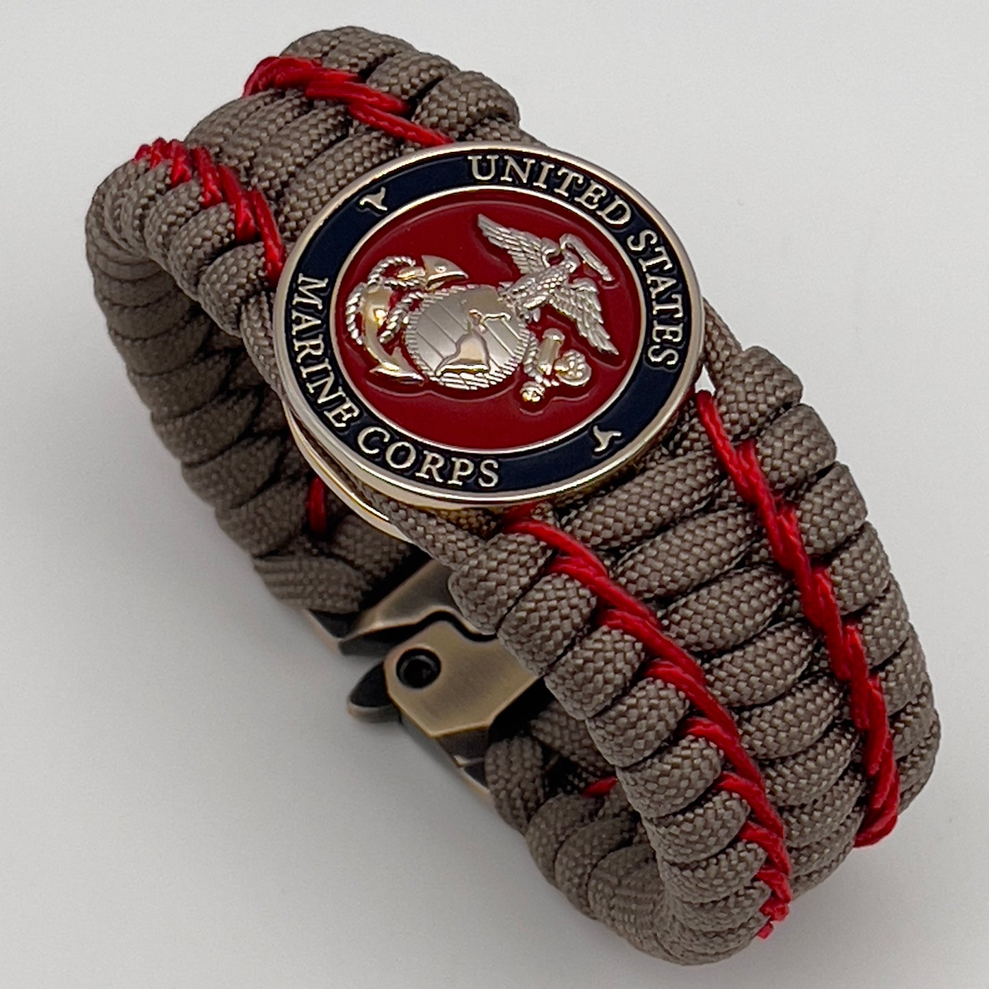 Thick, semi-rigid and comfortable braided United States Marine Corps bracelet featuring a 24K gold and silver plated USMC officer Eagle Globe and Anchor medallion, a gold Cobra style tactical buckle and woven with tan 550 paracord and Imperial Red micro cord.