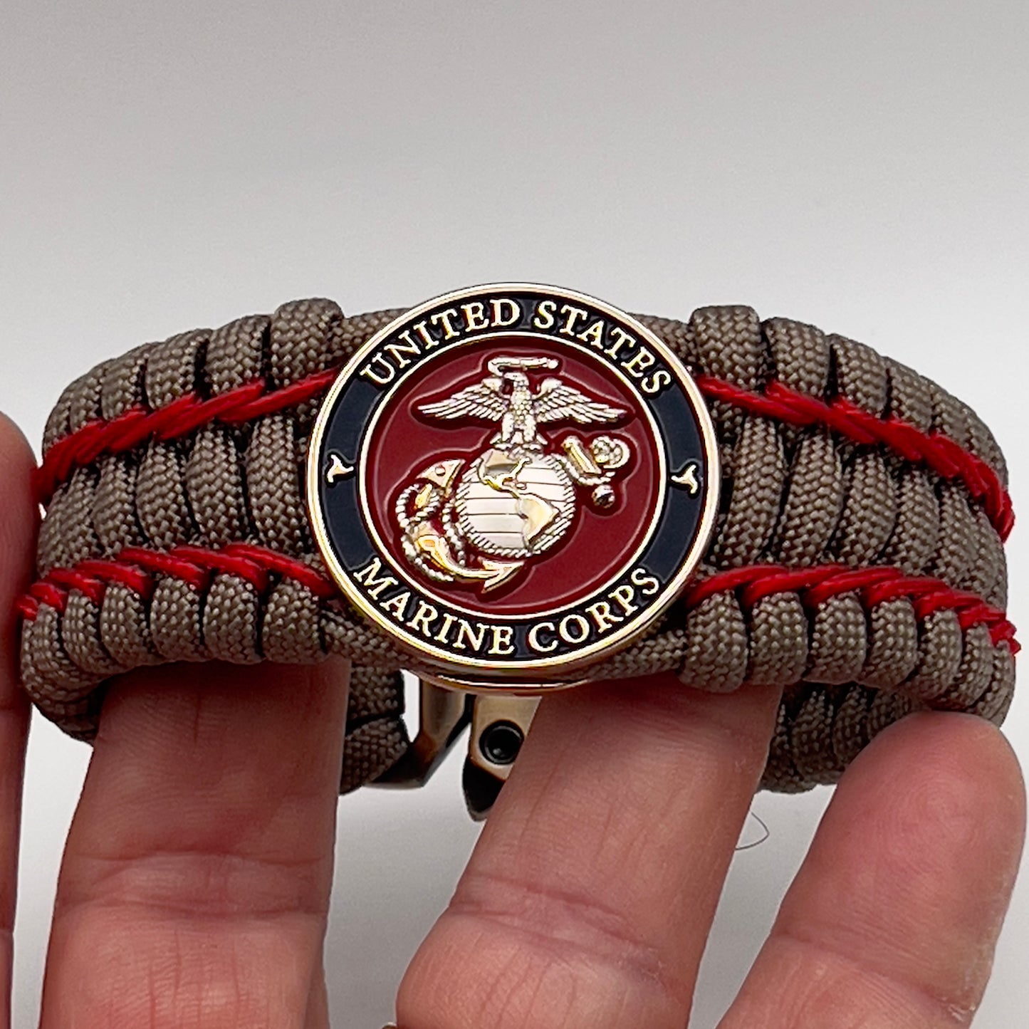 Thick, semi-rigid and comfortable braided United States Marine Corps bracelet featuring a 24K gold and silver plated USMC officer Eagle Globe and Anchor medallion, a gold Cobra style tactical buckle and woven with tan 550 paracord and Imperial Red micro cord.