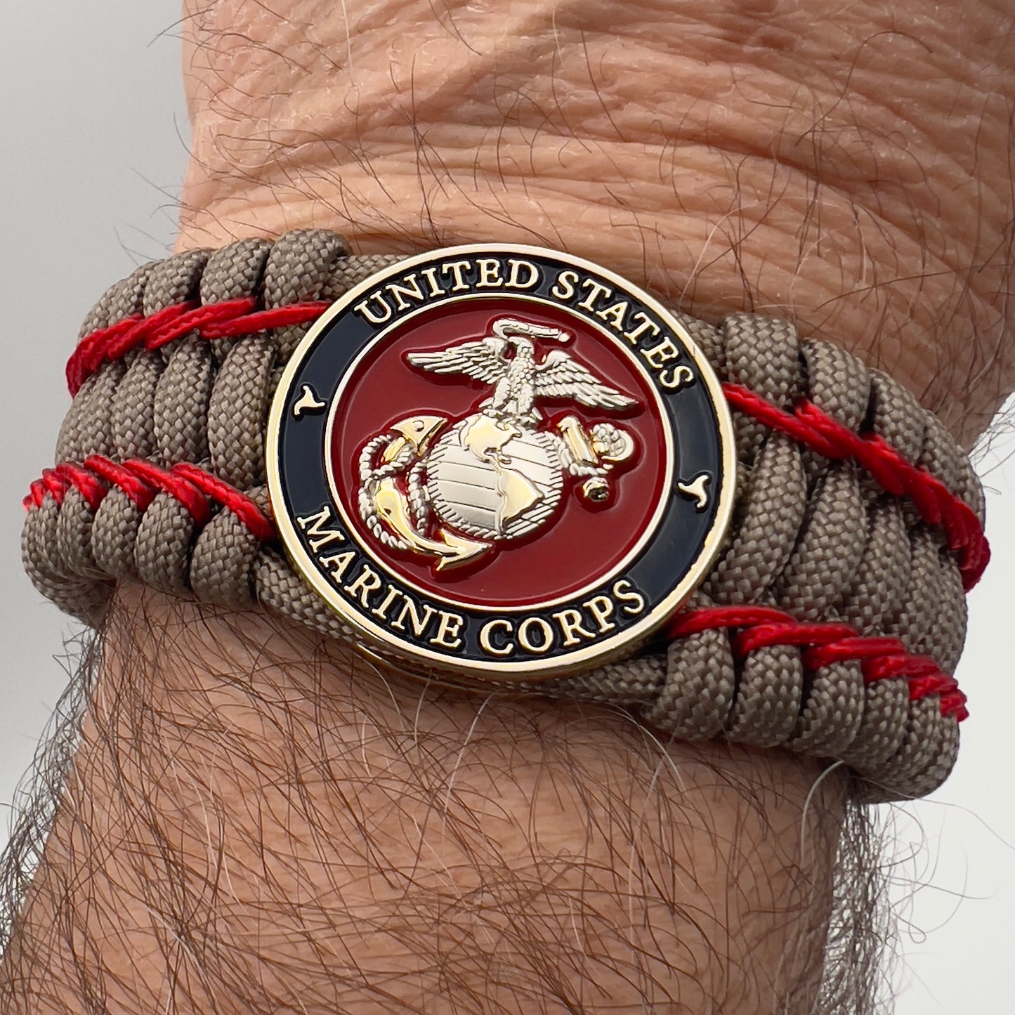 Thick, semi-rigid and comfortable braided United States Marine Corps bracelet featuring a 24K gold and silver plated USMC officer Eagle Globe and Anchor medallion, a gold Cobra style tactical buckle and woven with tan 550 paracord and Imperial Red micro cord.