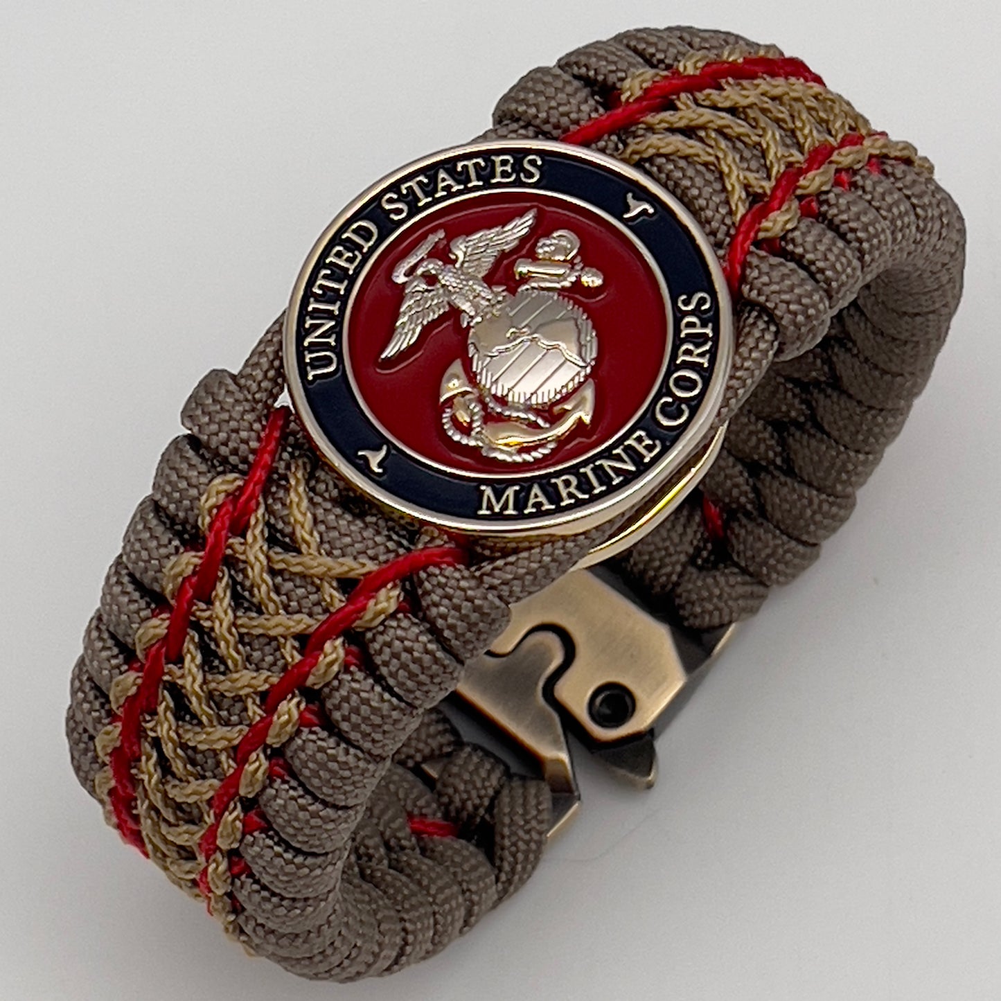Thick, semi-rigid and comfortable braided United States Marine Corps bracelet featuring a 24K gold and silver plated USMC officer Eagle Globe and Anchor medallion, a gold Cobra style tactical buckle and woven with tan 550 paracord and Imperial Red and gold micro cord.