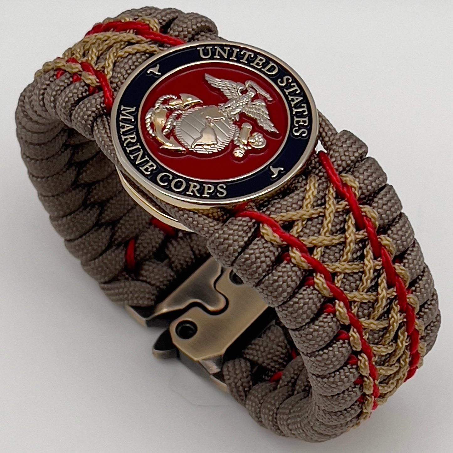 Thick, semi-rigid and comfortable braided United States Marine Corps bracelet featuring a 24K gold and silver plated USMC officer Eagle Globe and Anchor medallion, a gold Cobra style tactical buckle and woven with tan 550 paracord and Imperial Red and gold micro cord.