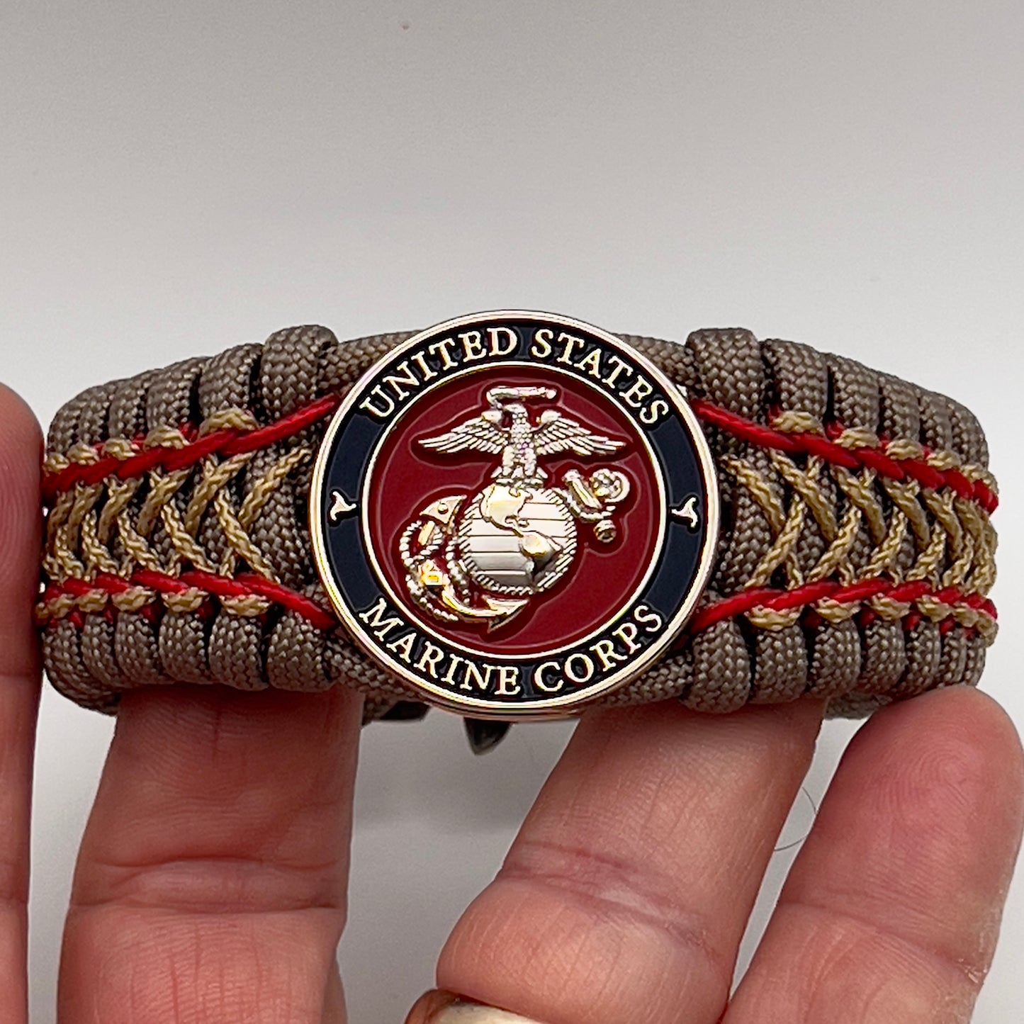Thick, semi-rigid and comfortable braided United States Marine Corps bracelet featuring a 24K gold and silver plated USMC officer Eagle Globe and Anchor medallion, a gold Cobra style tactical buckle and woven with tan 550 paracord and Imperial Red and gold micro cord.