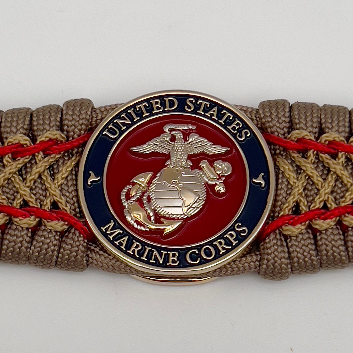 Thick, semi-rigid and comfortable braided United States Marine Corps bracelet featuring a 24K gold and silver plated USMC officer Eagle Globe and Anchor medallion, a gold Cobra style tactical buckle and woven with tan 550 paracord and Imperial Red and gold micro cord.