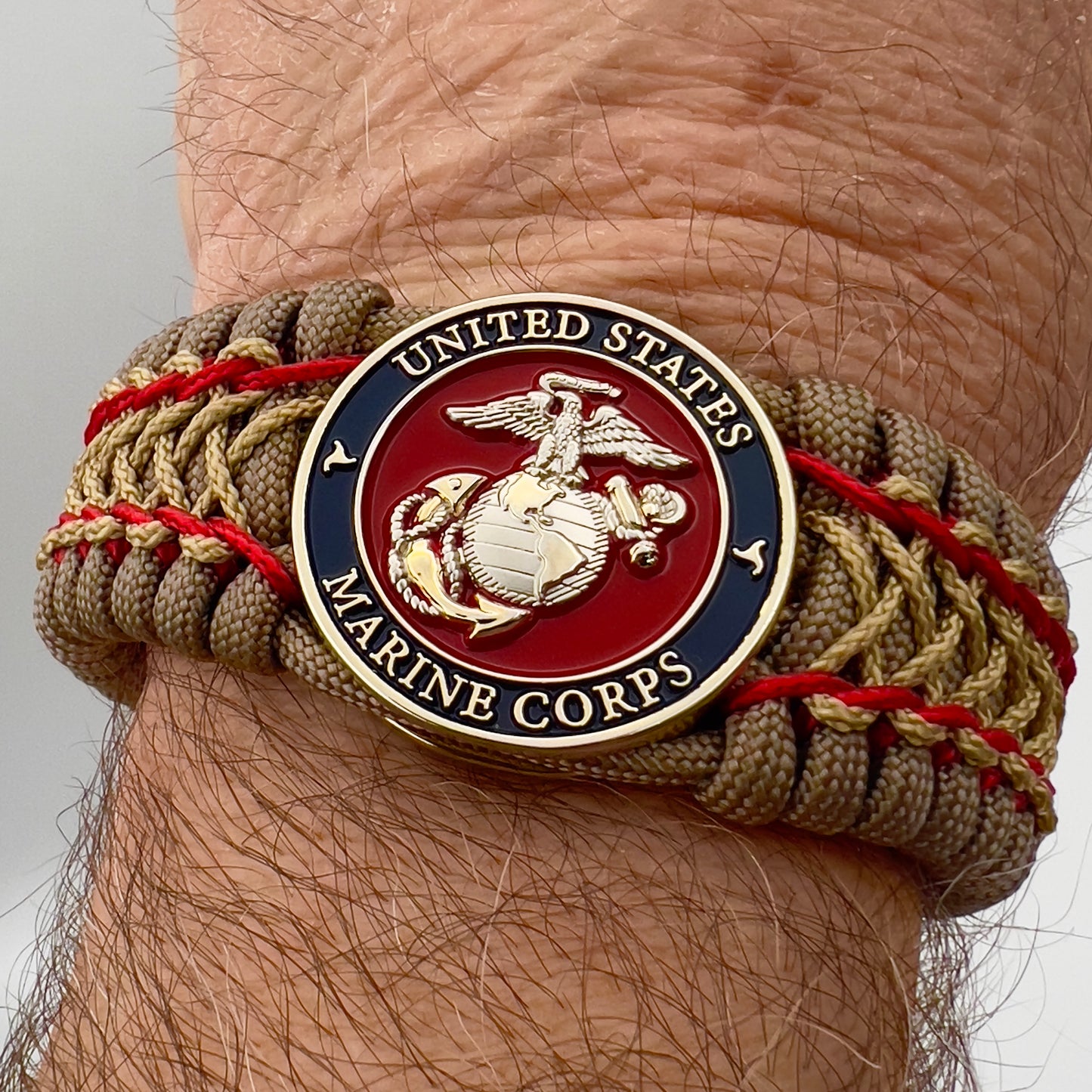 Thick, semi-rigid and comfortable braided United States Marine Corps bracelet featuring a 24K gold and silver plated USMC officer Eagle Globe and Anchor medallion, a gold Cobra style tactical buckle and woven with tan 550 paracord and Imperial Red and gold micro cord.