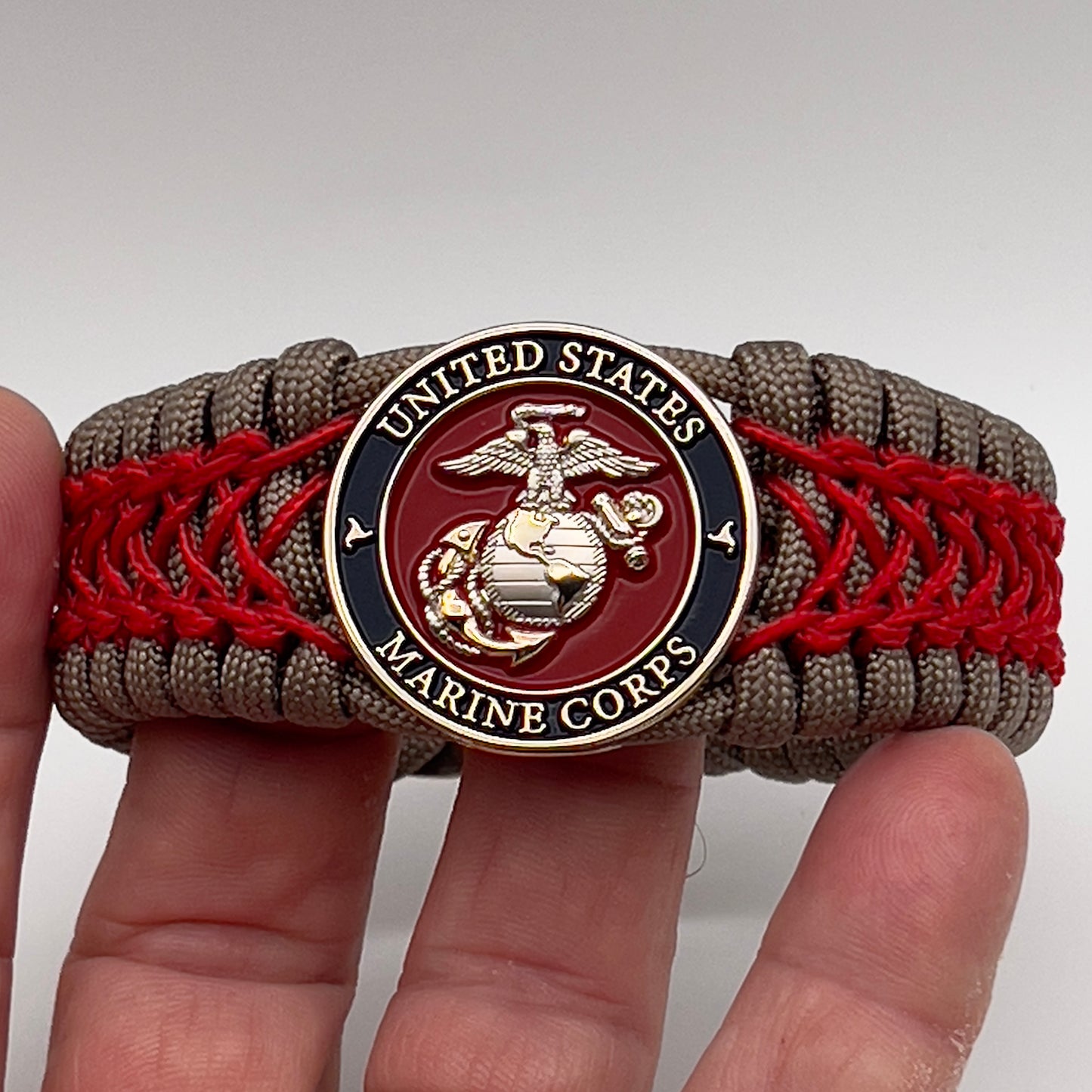 Thick, semi-rigid and comfortable braided United States Marine Corps bracelet featuring a 24K gold and silver plated USMC officer Eagle Globe and Anchor medallion, a gold Cobra style tactical buckle and woven with tan 550 paracord and Imperial red micro cord.
