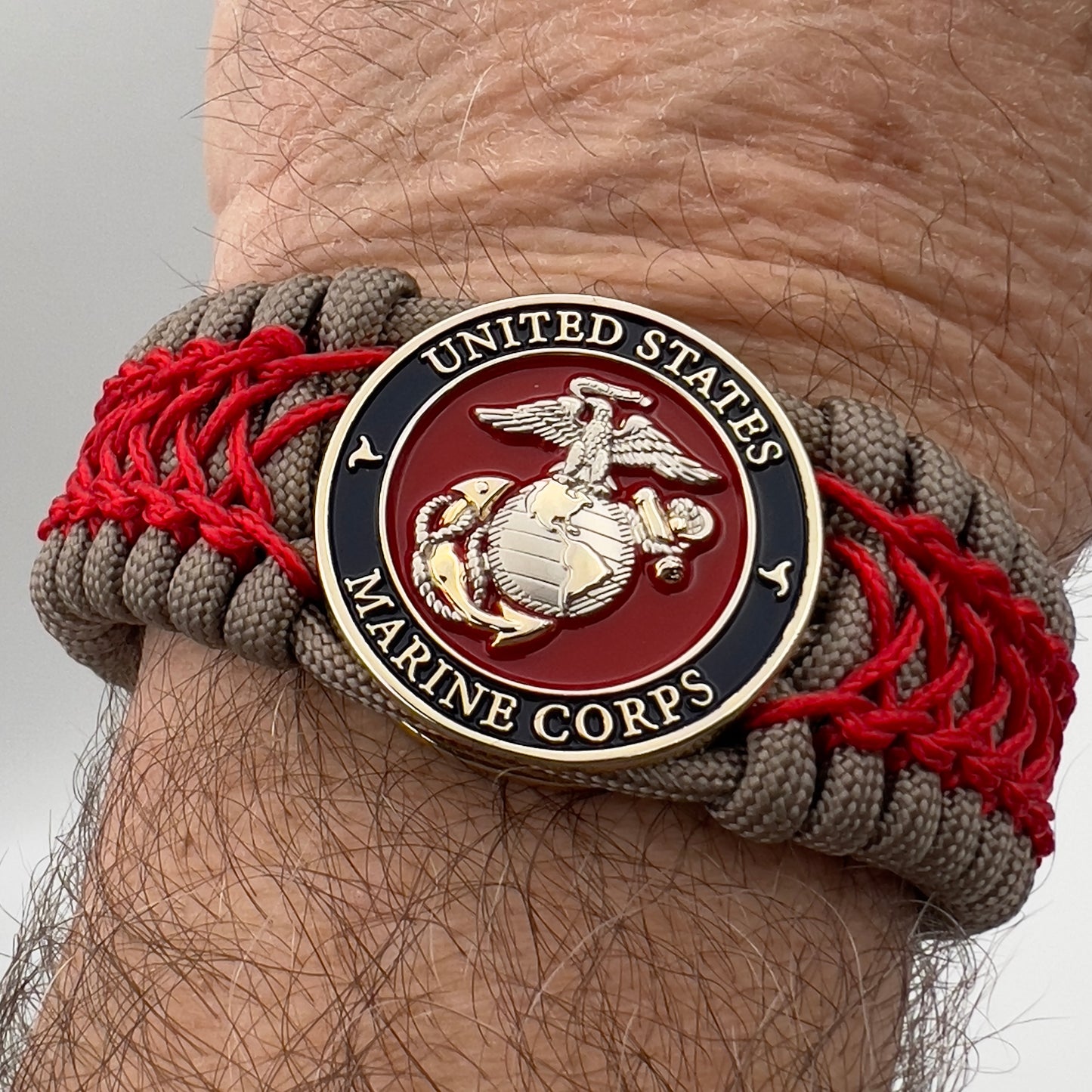 Thick, semi-rigid and comfortable braided United States Marine Corps bracelet featuring a 24K gold and silver plated USMC officer Eagle Globe and Anchor medallion, a gold Cobra style tactical buckle and woven with tan 550 paracord and Imperial red micro cord.