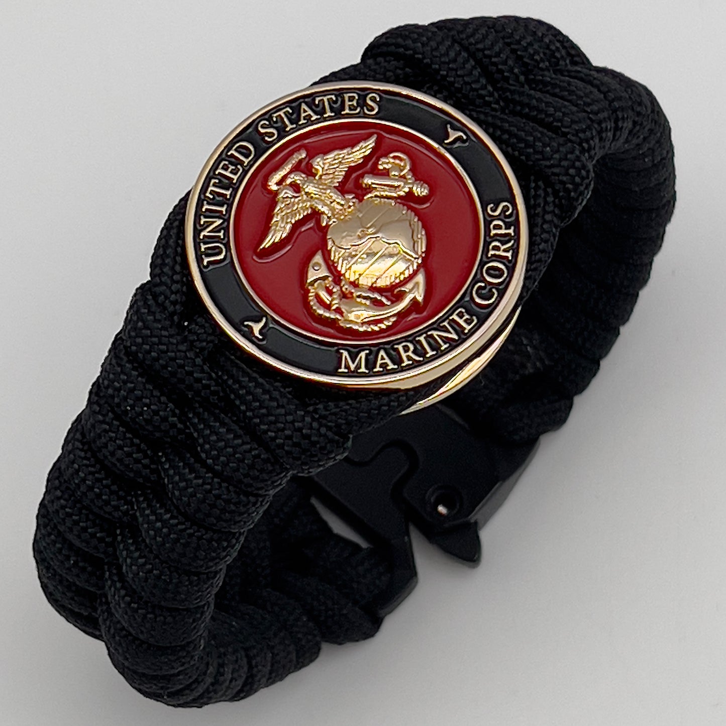Thick, semi-rigid and comfortable braided United States Marine Corps bracelet featuring a 24K gold plated USMC officer Eagle Globe and Anchor medallion, a black Cobra style tactical buckle and woven with black 550 paracord.