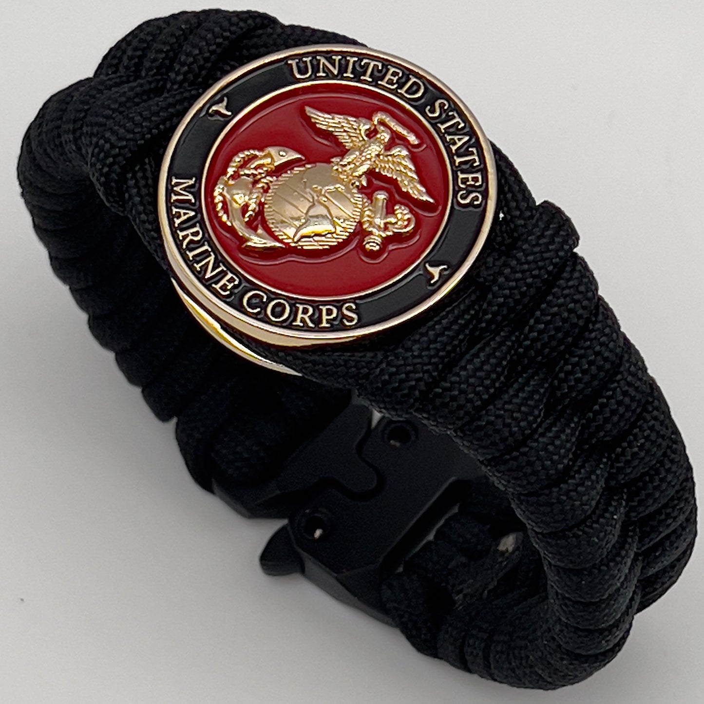 Thick, semi-rigid and comfortable braided United States Marine Corps bracelet featuring a 24K gold plated USMC officer Eagle Globe and Anchor medallion, a black Cobra style tactical buckle and woven with black 550 paracord.