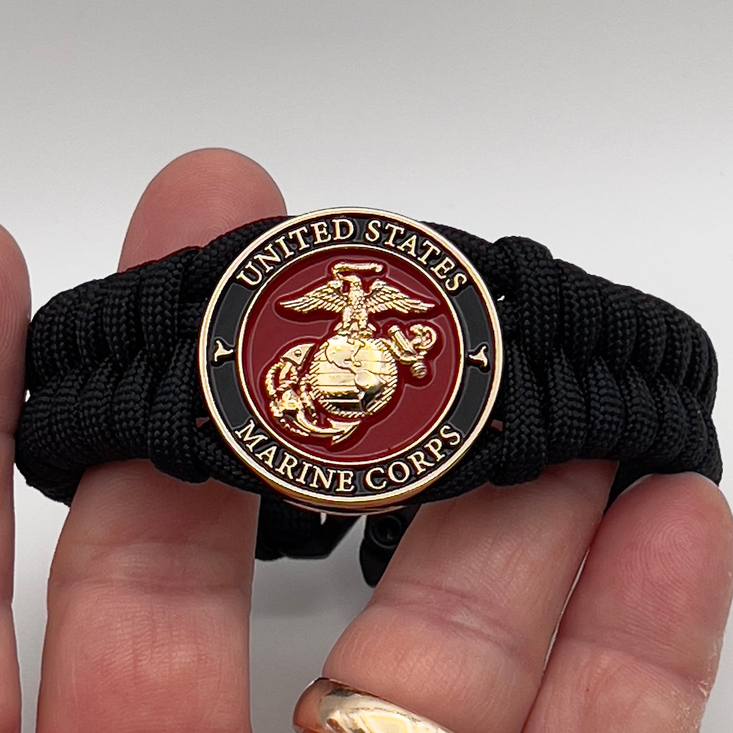 Thick, semi-rigid and comfortable braided United States Marine Corps bracelet featuring a 24K gold plated USMC officer Eagle Globe and Anchor medallion, a black Cobra style tactical buckle and woven with black 550 paracord.