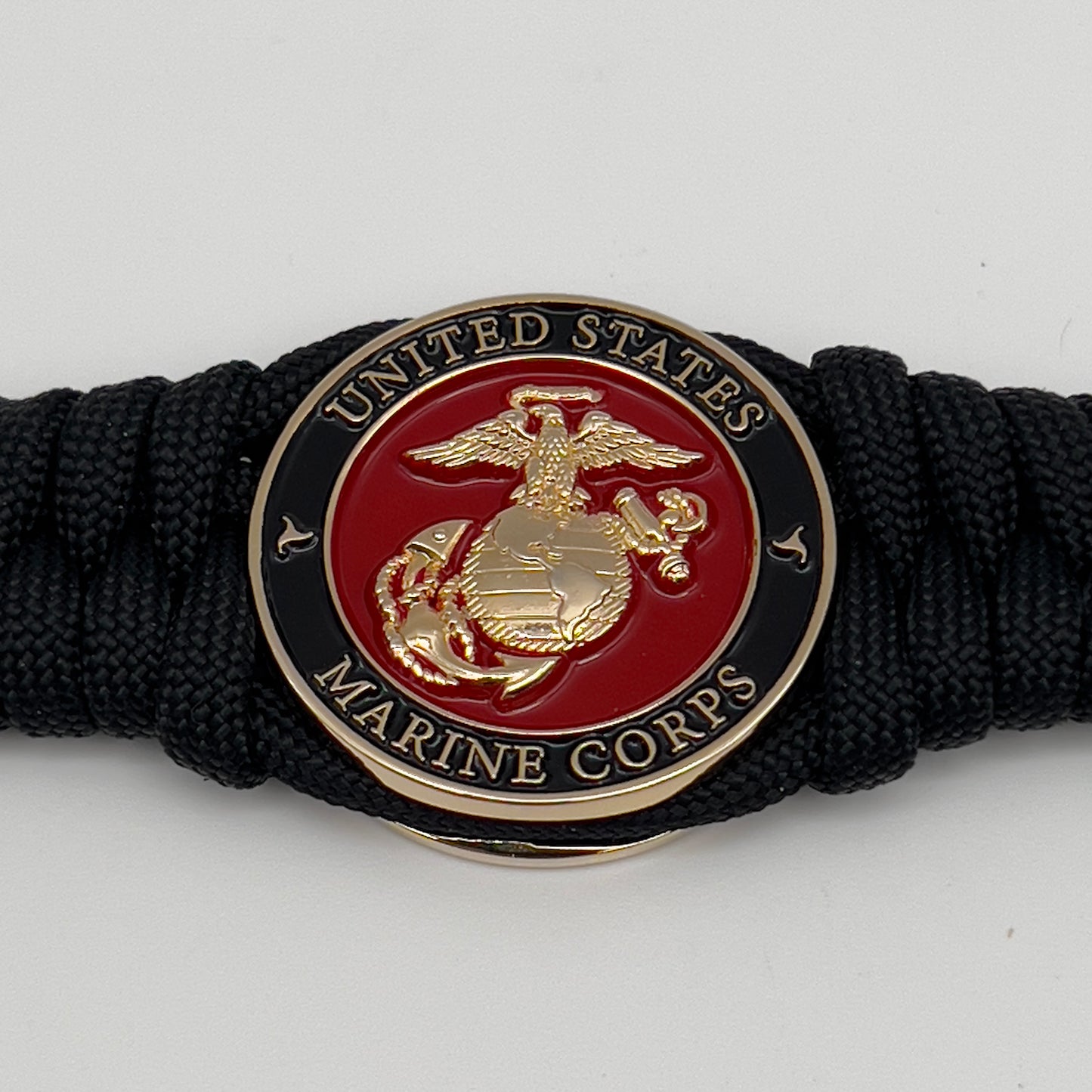 Thick, semi-rigid and comfortable braided United States Marine Corps bracelet featuring a 24K gold plated USMC officer Eagle Globe and Anchor medallion, a black Cobra style tactical buckle and woven with black 550 paracord.
