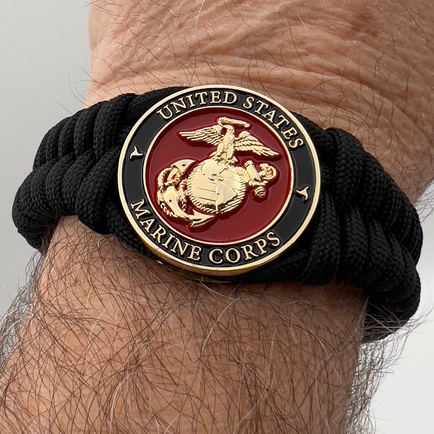 Thick, semi-rigid and comfortable braided United States Marine Corps bracelet featuring a 24K gold plated USMC officer Eagle Globe and Anchor medallion, a black Cobra style tactical buckle and woven with black 550 paracord.