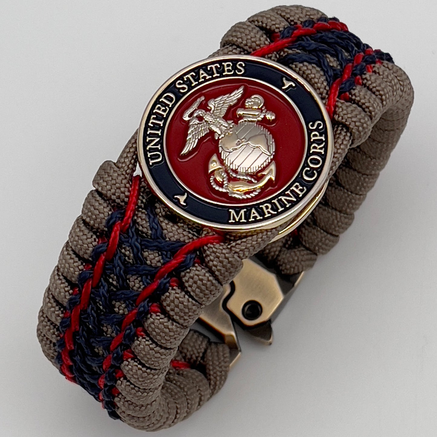 Thick, rigid and comfortable braided United States Marine Corps bracelet featuring a 24K gold and silver plated USMC officer Eagle Globe and Anchor medallion, a gold Cobra style tactical buckle and woven with tan 550 paracord and Imperial Red and Navy Blue micro cord.