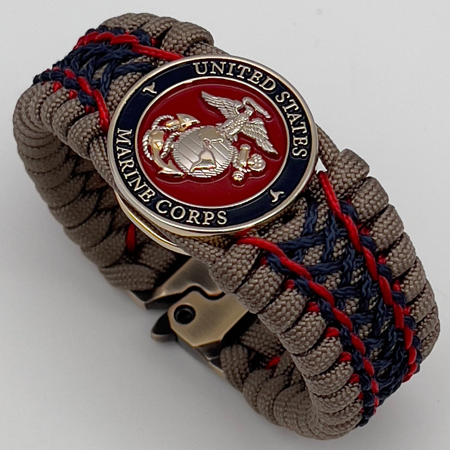 Thick, rigid and comfortable braided United States Marine Corps bracelet featuring a 24K gold and silver plated USMC officer Eagle Globe and Anchor medallion, a gold Cobra style tactical buckle and woven with tan 550 paracord and Imperial Red and Navy Blue micro cord.